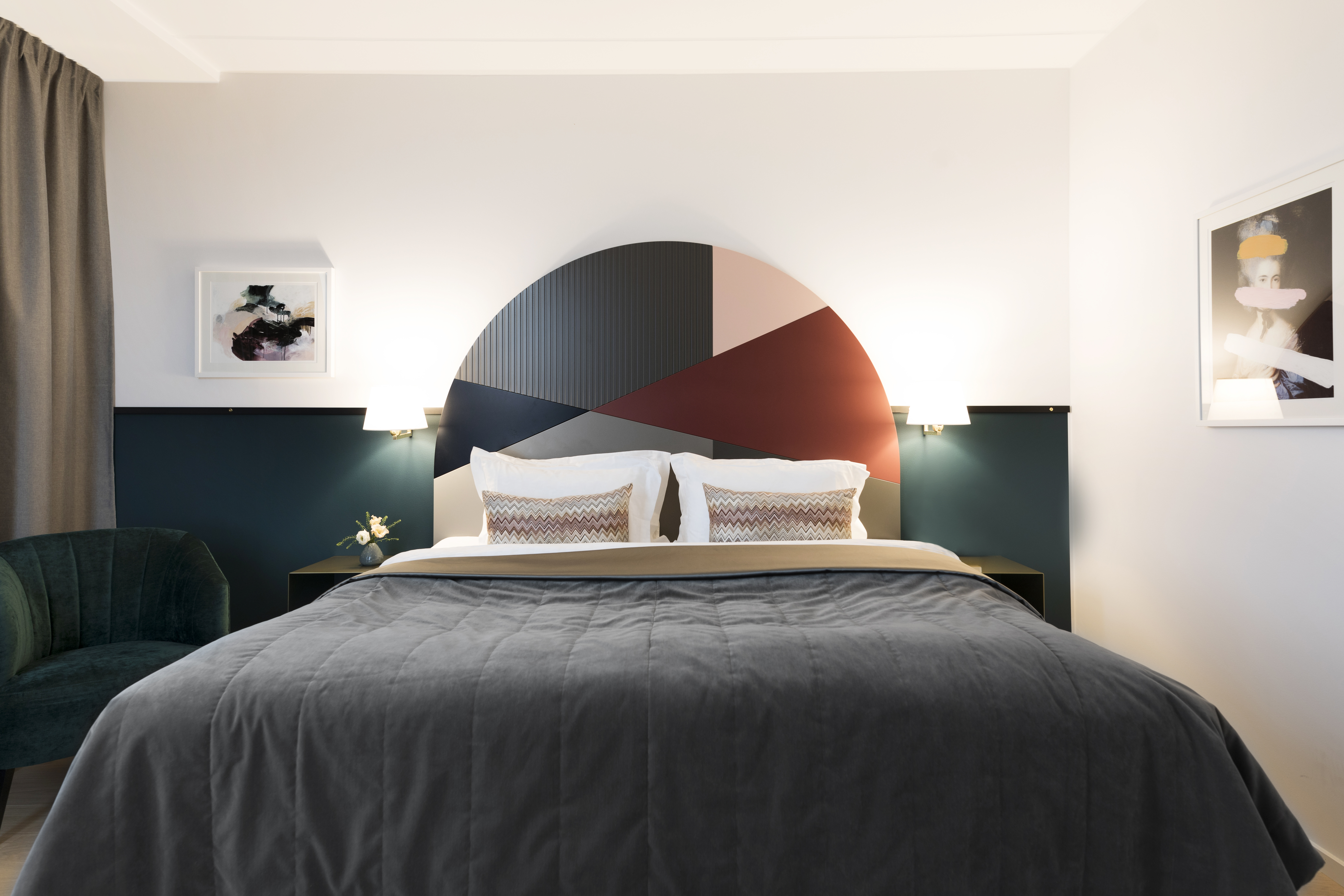Ljust hotellrum med säng, färgglad sänggavel och sänglampor