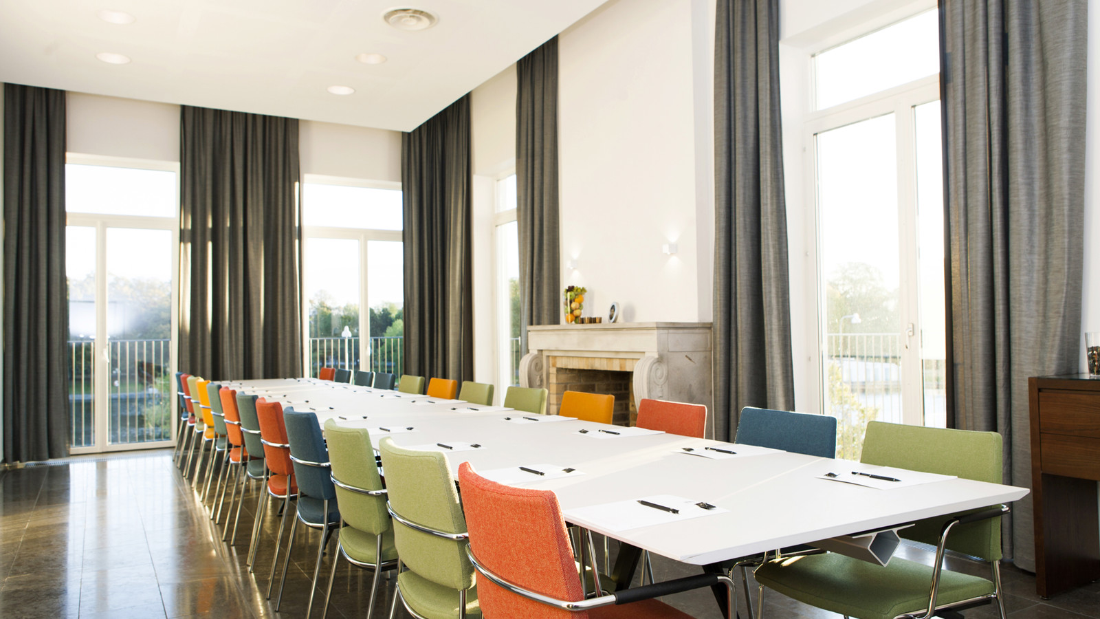 Big table with colourful chairs and grey curtains