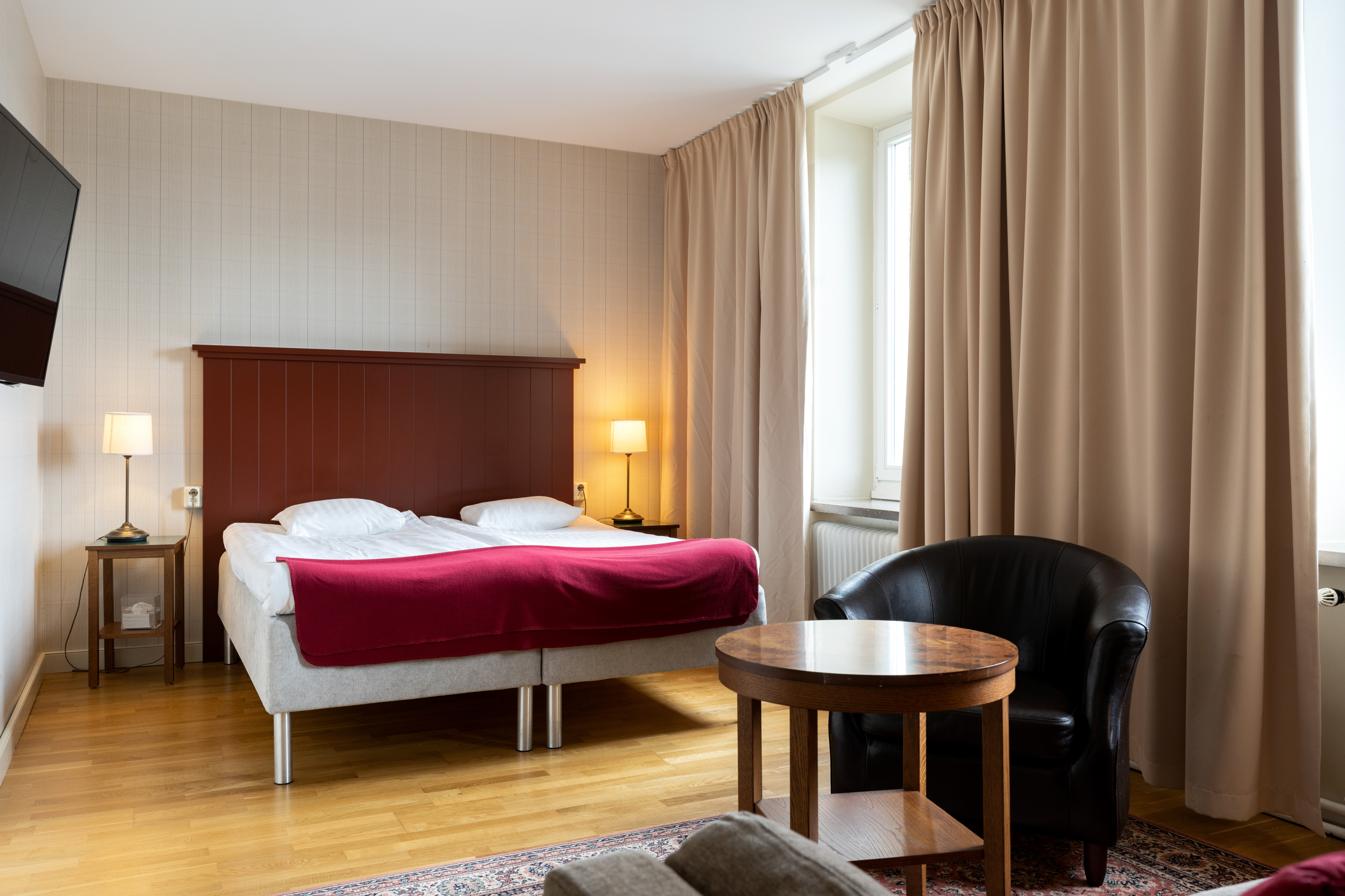 Mysigt hotellrum med säng, sänggavel i trä och svart läderfåtölj