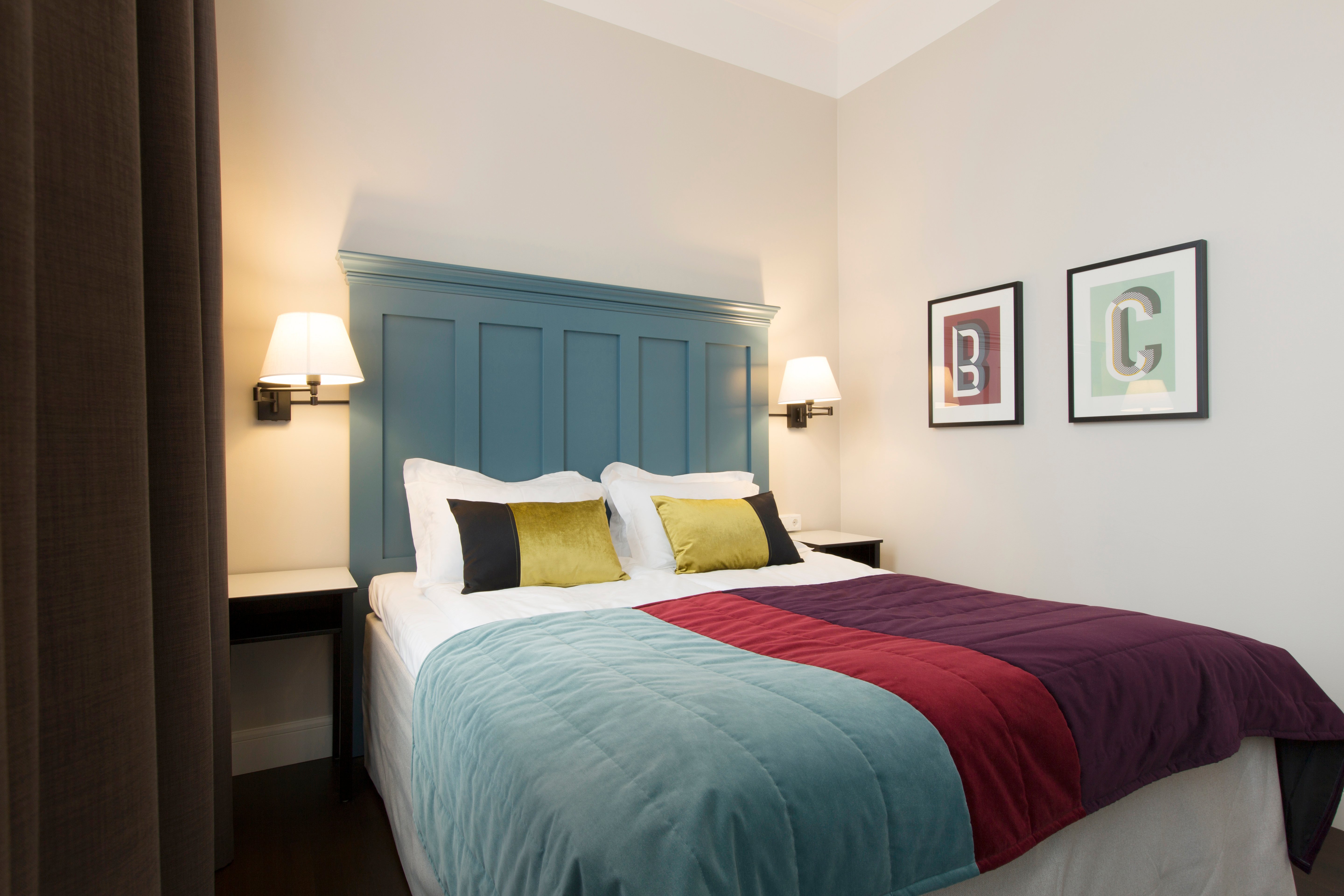 Ljust hotellrum med säng, stor blå sänggavel och sängtavlor
