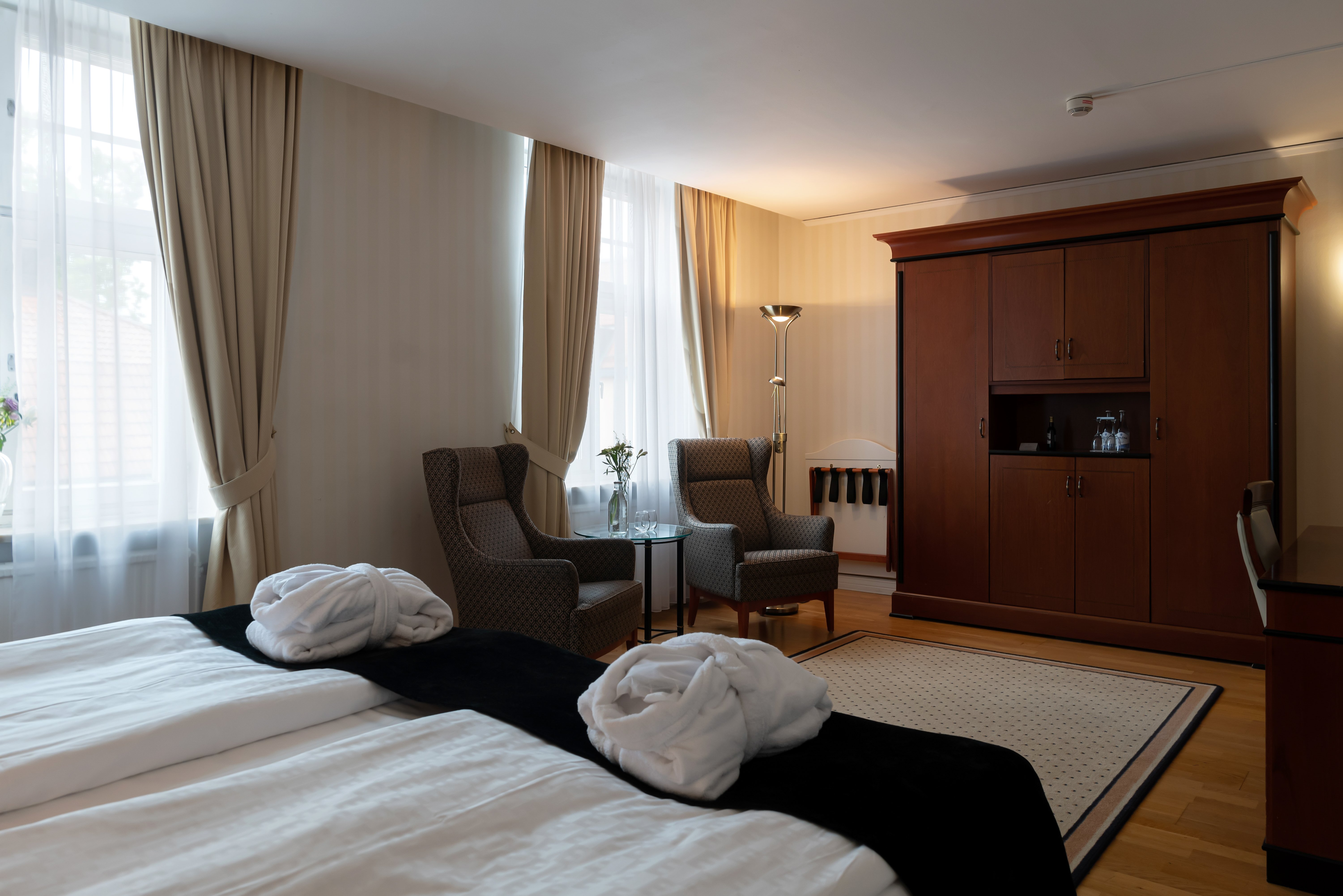 Mysigt hotellrum med morgonrock på säng, garderob och fåtöljer