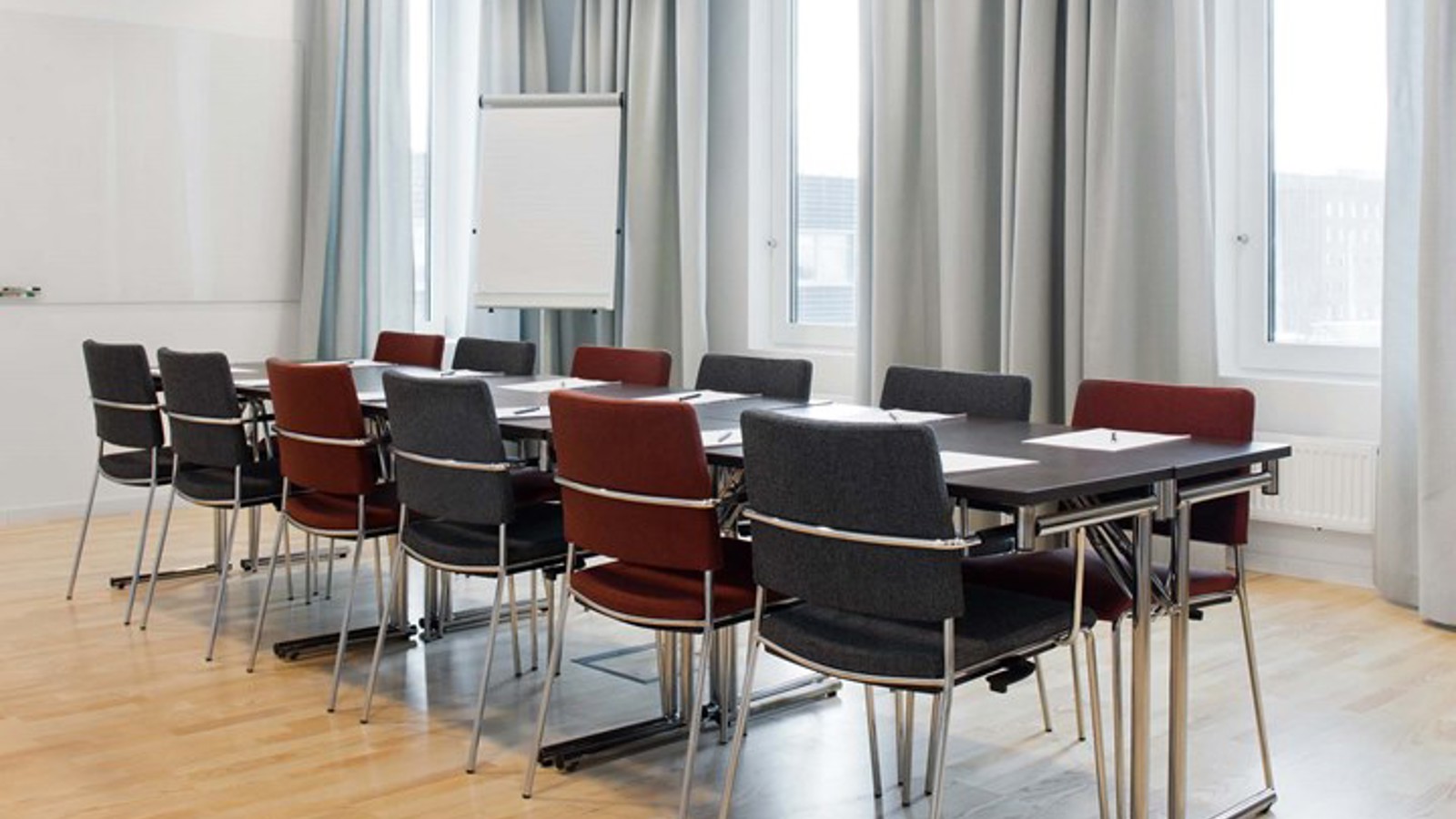 Konferensrum med styrelsesittning, stora fönster, grå gardiner och mörka stolar
