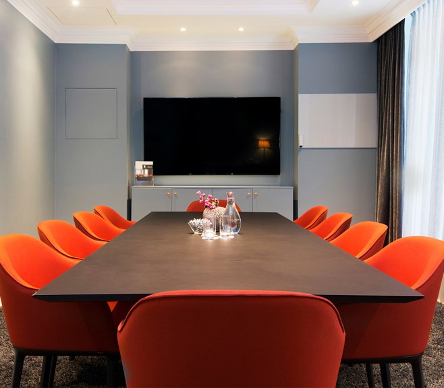 Board room with dark brown table, red chairs and blue walls