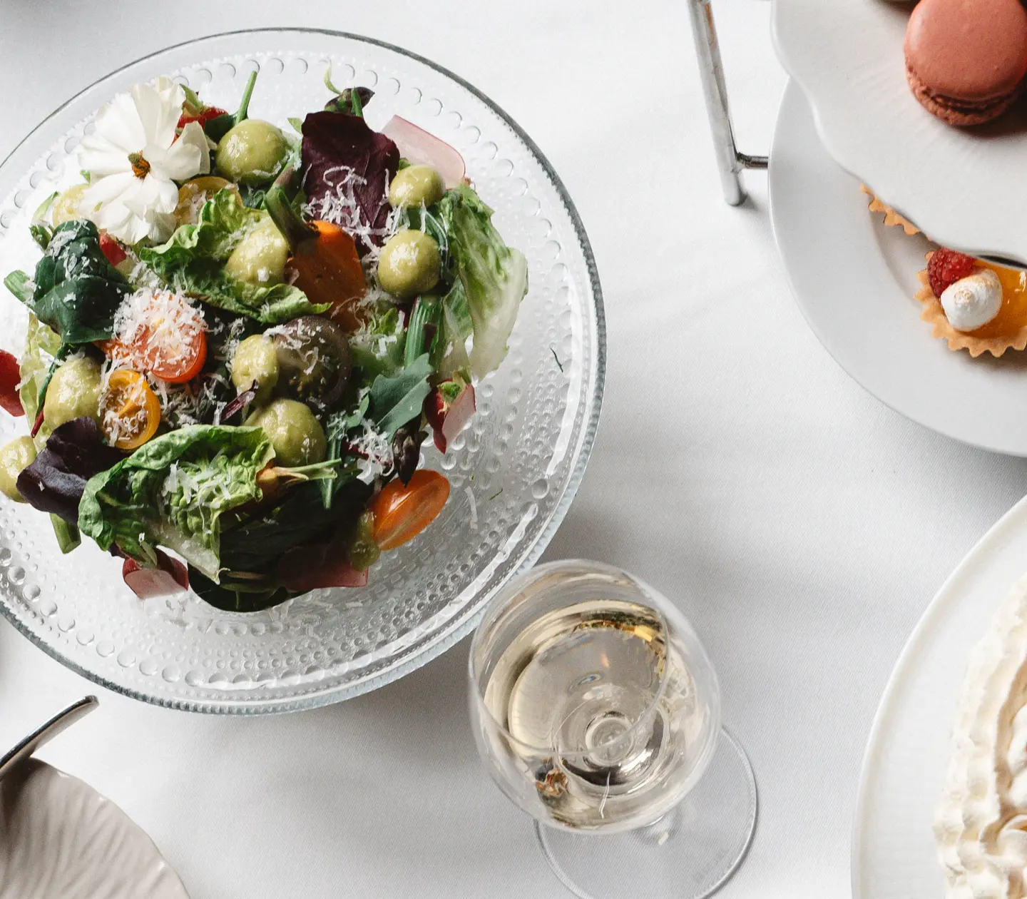 Buffé med lax, sallad, macarons, jordgubbstårta och små kakor på ett bord, serverad med ett glas vitt vin.