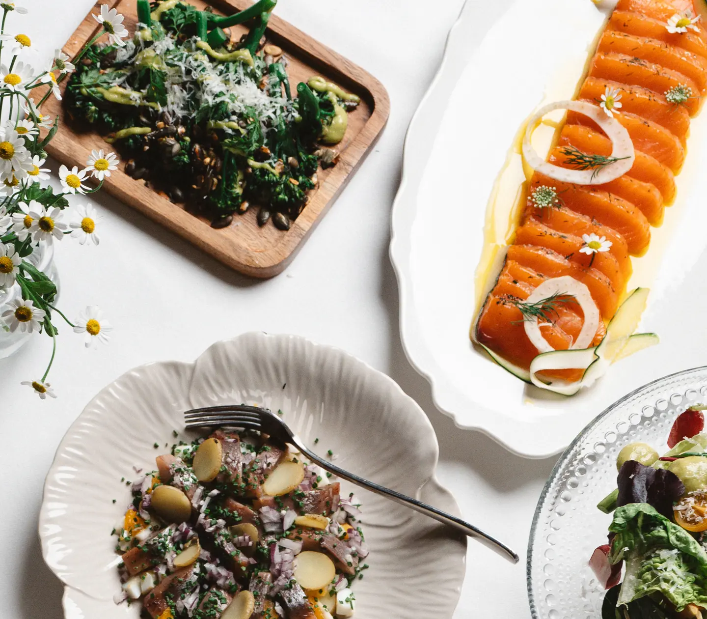 Svenskt smörgåsbord med rökta laxskivor, färsk sallad, ostar, bröd och grönsaksrätt på ett snyggt dukat bord med blommor.
