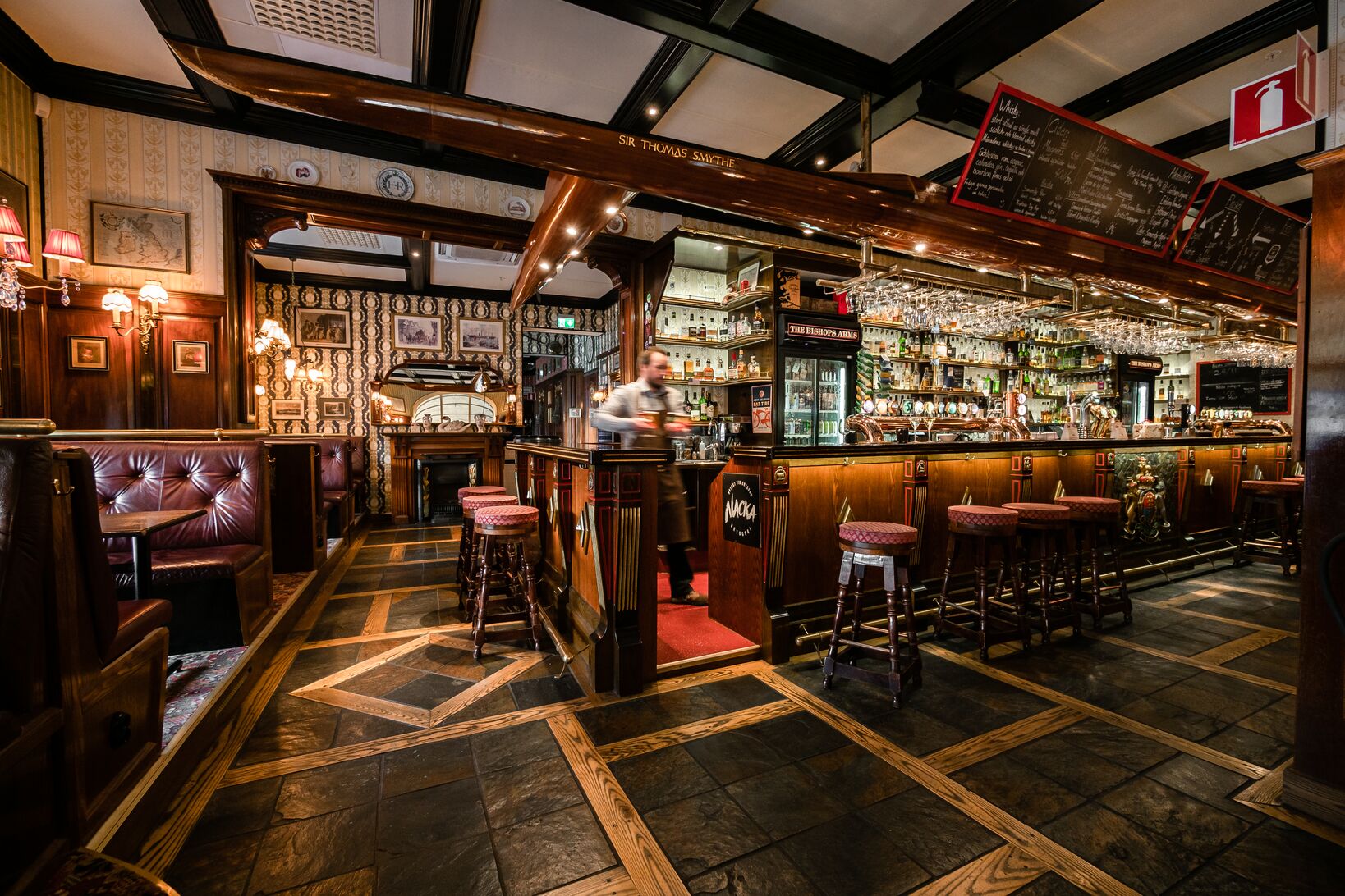 Interiör av en traditionell pub med träinredning, bardisk, högstolar och stämningsfull belysning.