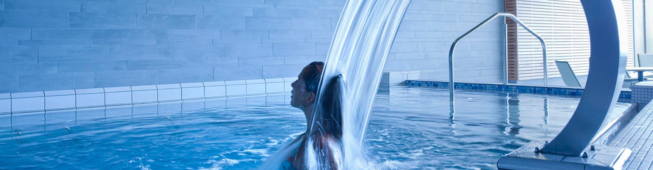 Kvinna står under en vattenfallsfontän i en pool