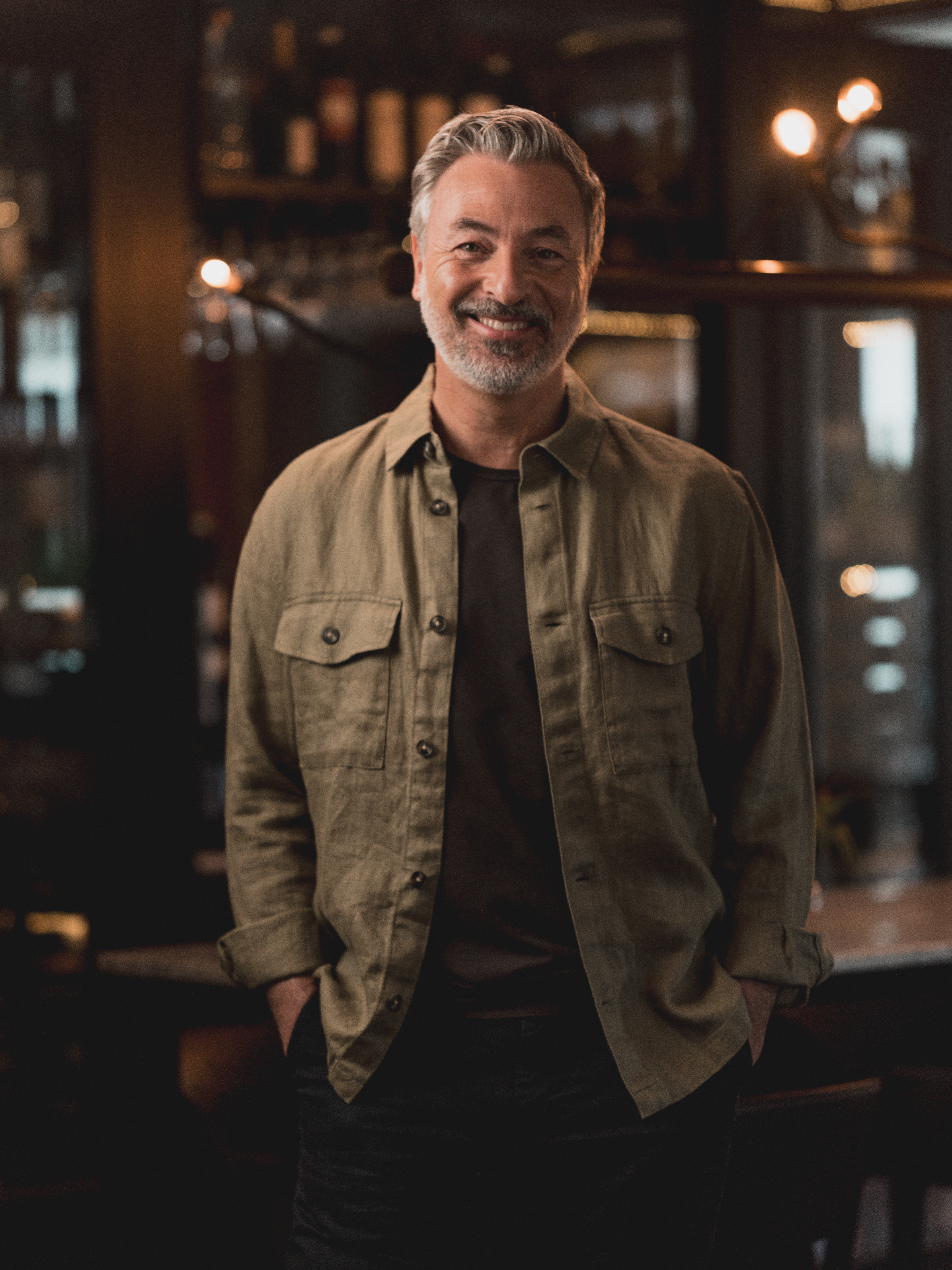 Tareq Taylor i grön skjorta ler inomhus i avslappnad miljö.