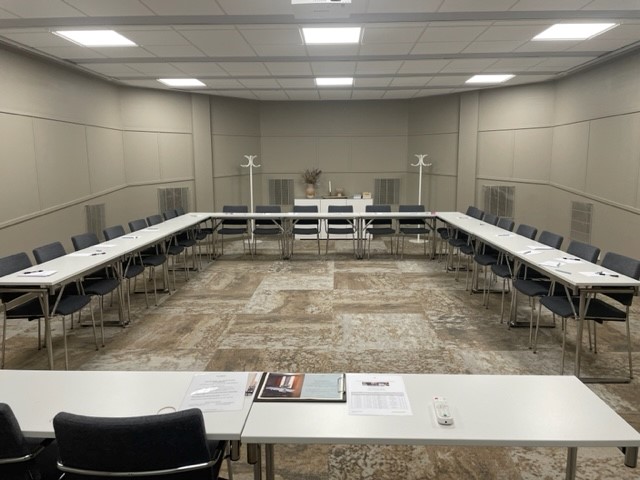 Konferenslokal med skolsittning, mörka stolar och grå väggar