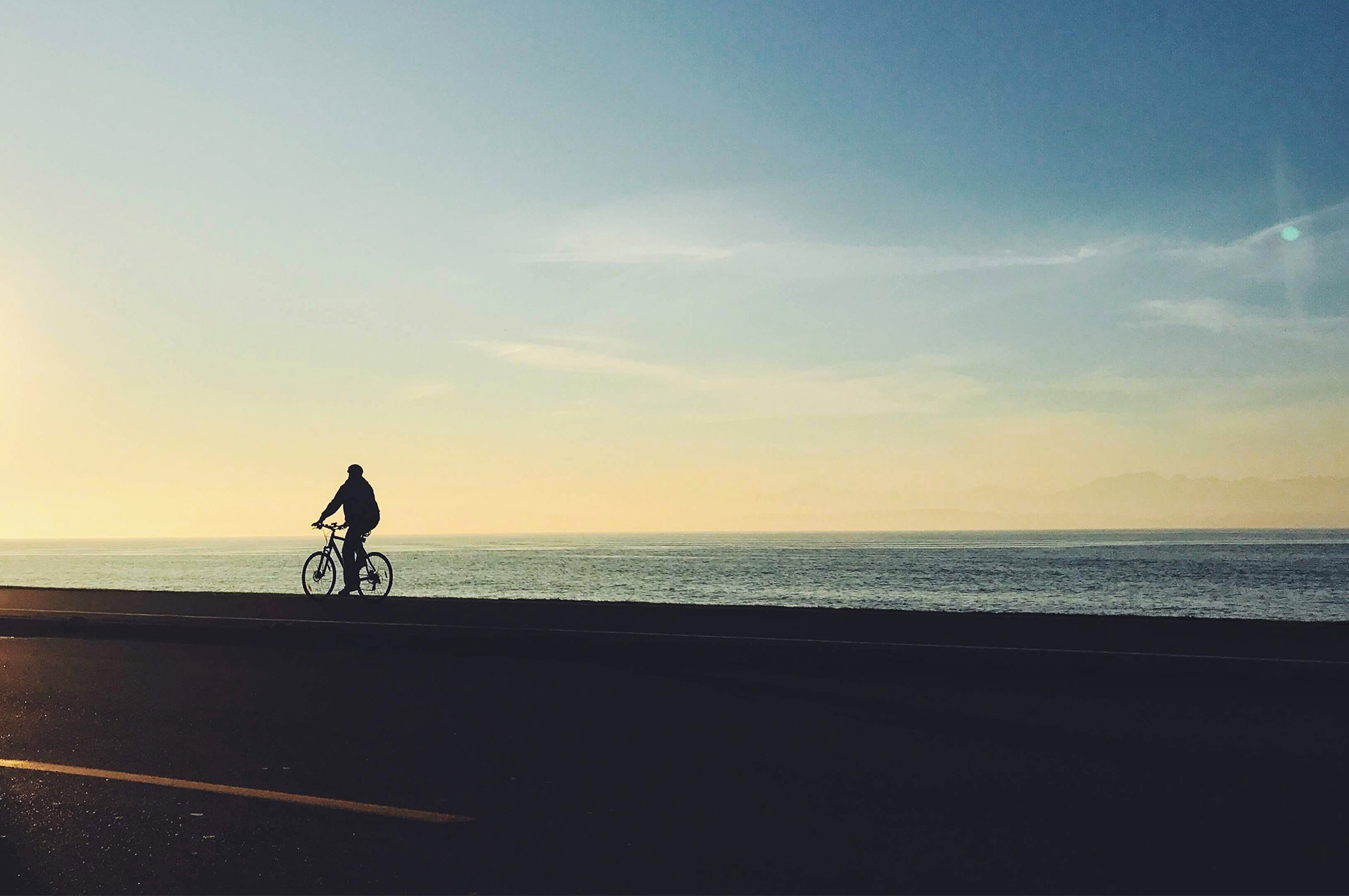 En person som cyklar längs havet i solnedgångsljus