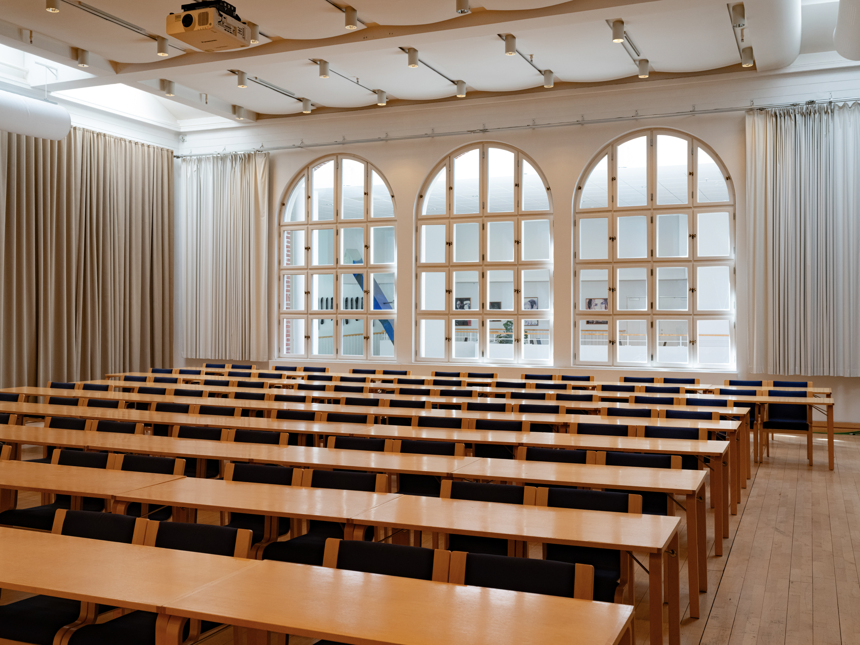 Konferenssal med biosittning, stolar i trä, trägolv och vita väggar