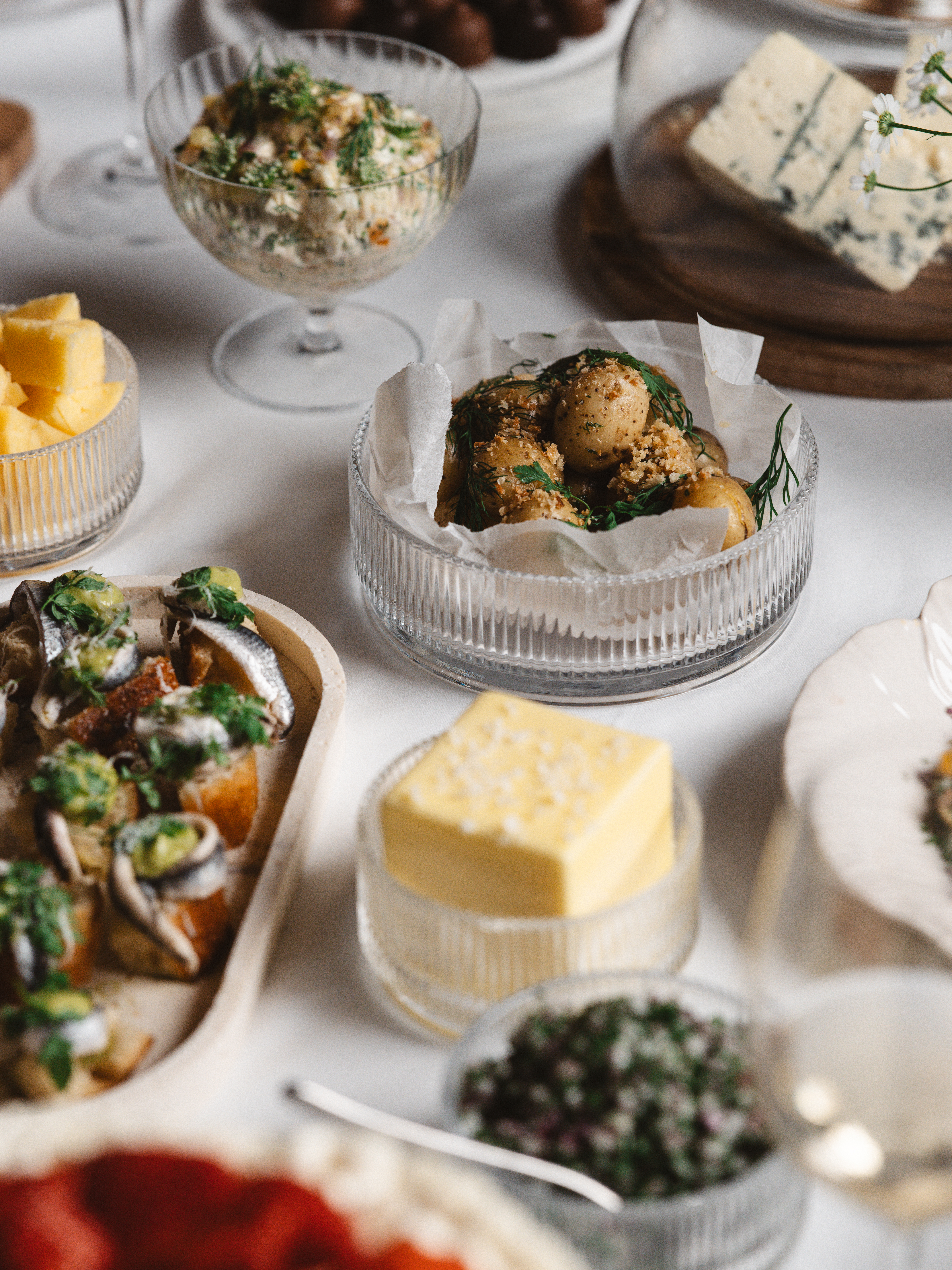 Traditionell svensk buffé med sill, smör, potatis, ost och andra festliga maträtter på ett dukat bord.
