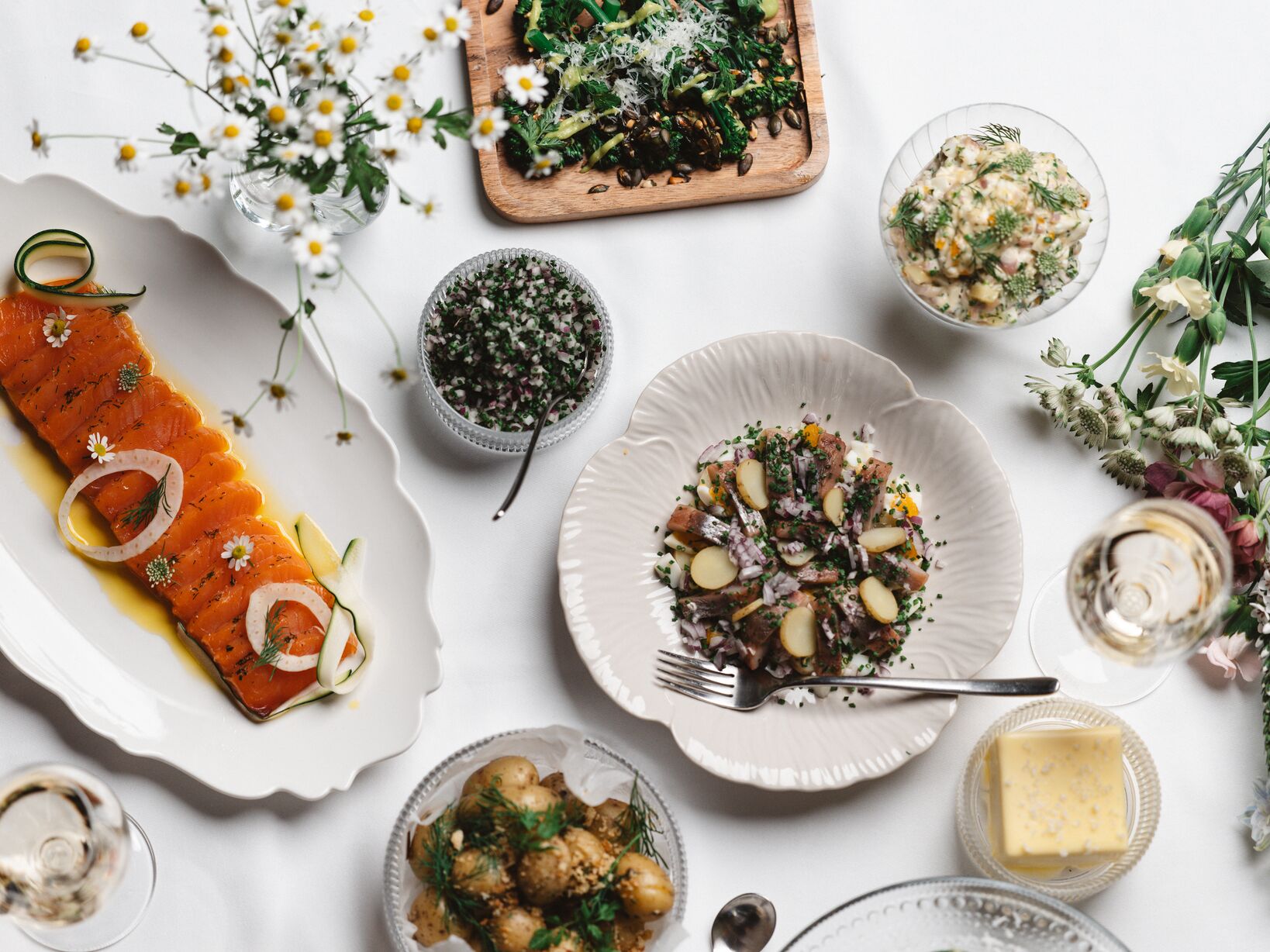 Svensk traditionell midsommarmat med gravad lax, sill, färskpotatis, grönsaker och örter på ett dukat bord.