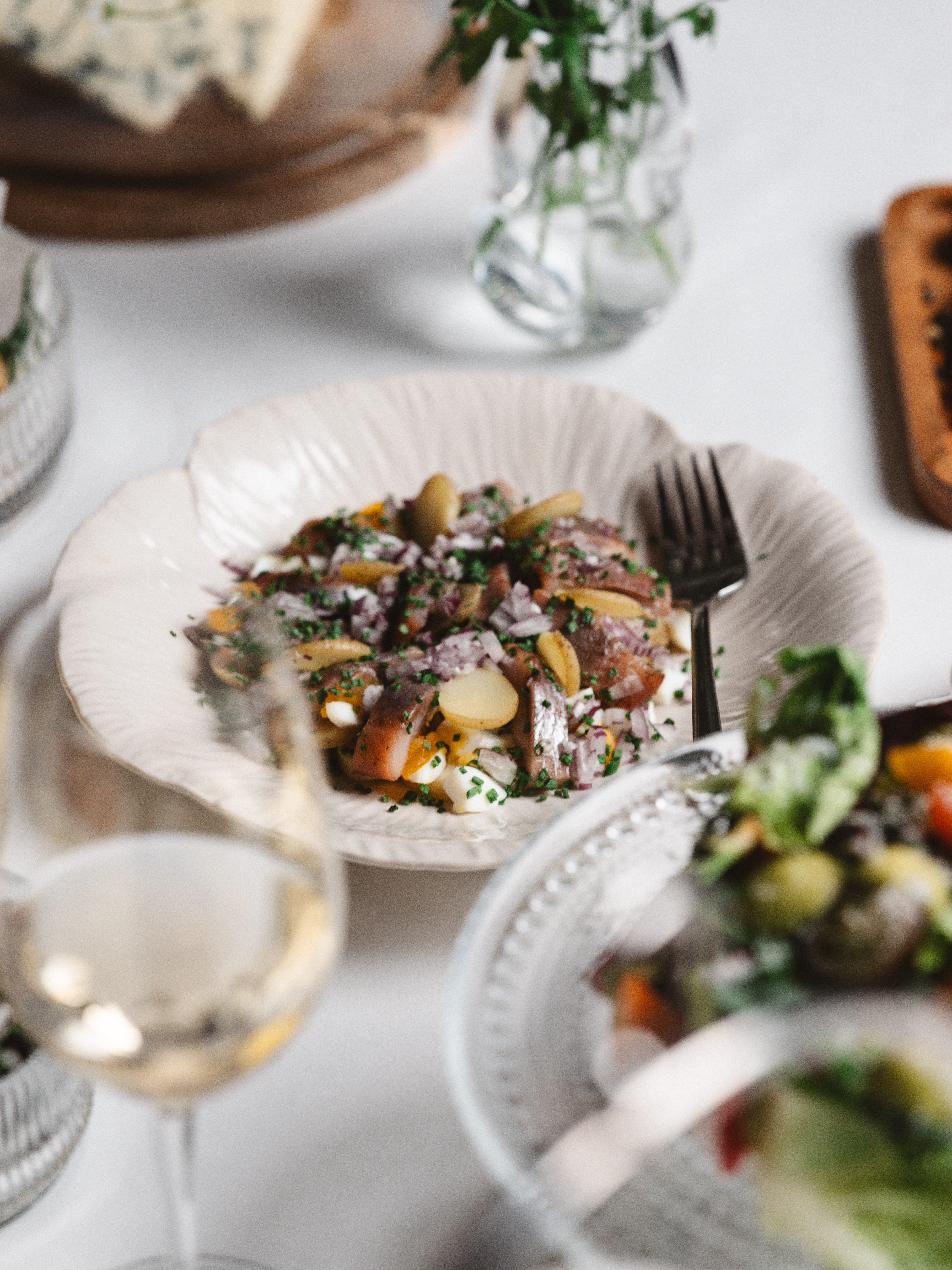 Maträtt med potatis, lök, örter och vin på bord.