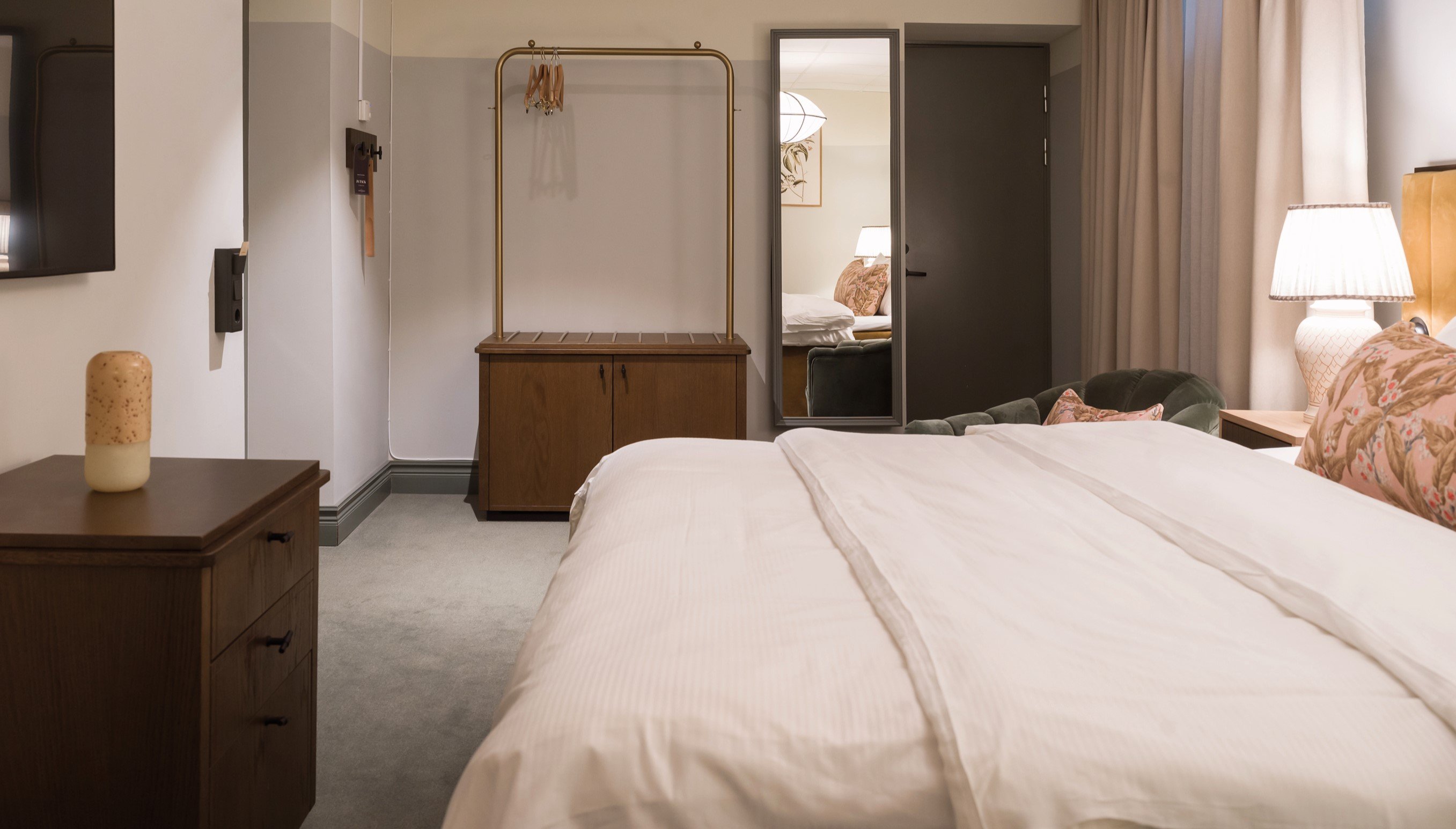 Modernt hotellrum med en stor säng, elegant belysning och inredning i varma toner