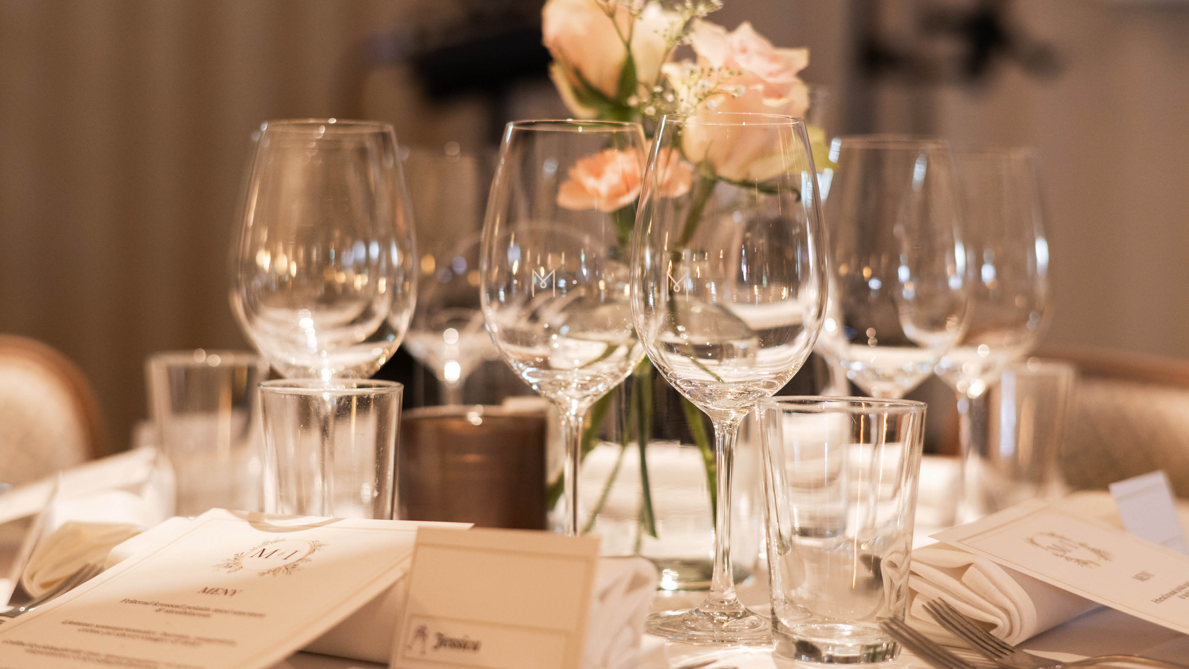 Serveringsvagn med marmorskivor, dekorerad med vinflaskor och glas, omgiven av blomsterarrangemang med rosor och grönt.