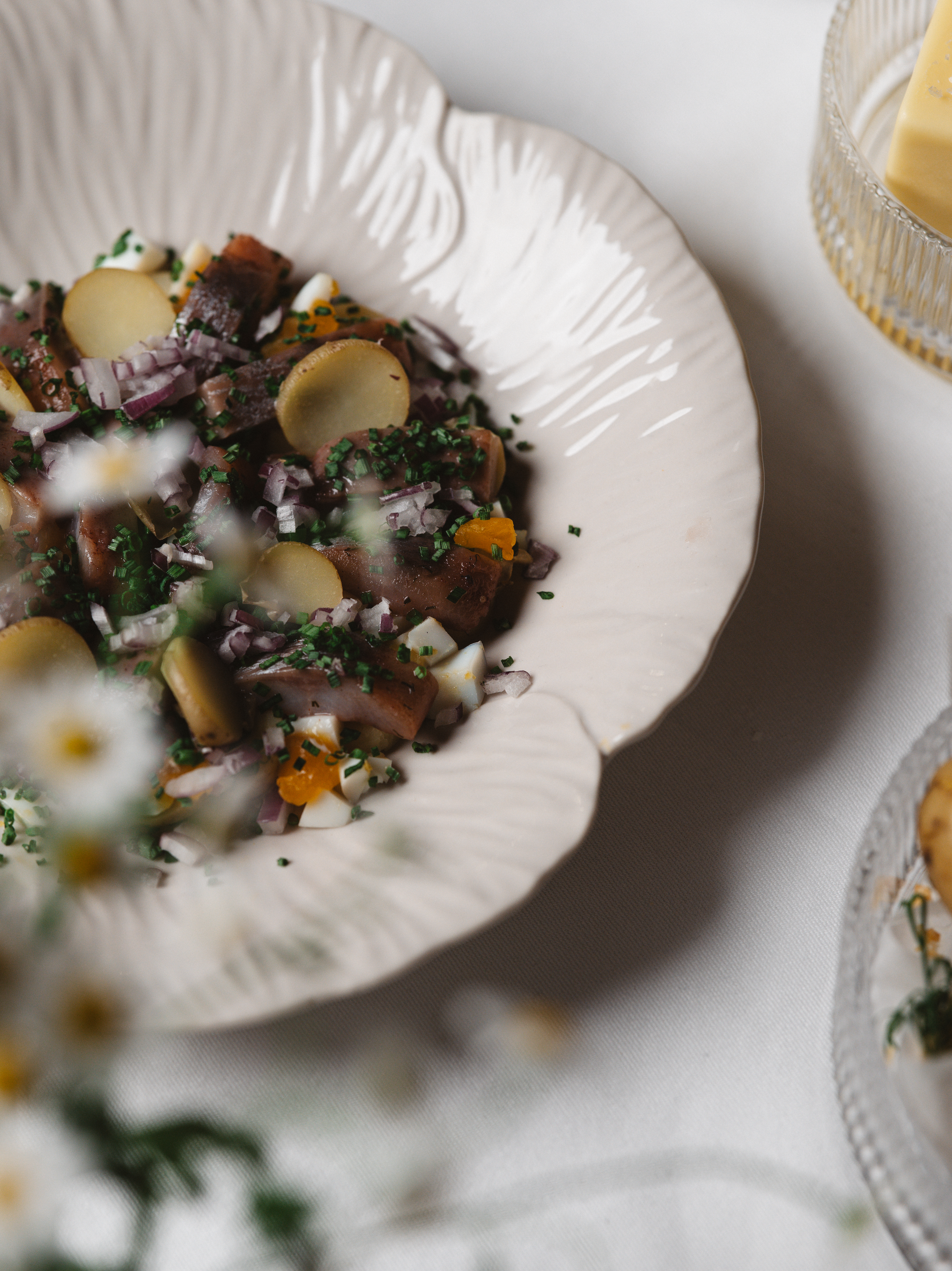 Traditionell svensk potatissallad med färska örter, rödlök och ägg i en vit tallrik.