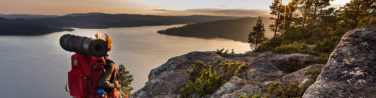 En kvinna med vandrarutrustning går på ett berg med utsikt över en sjö