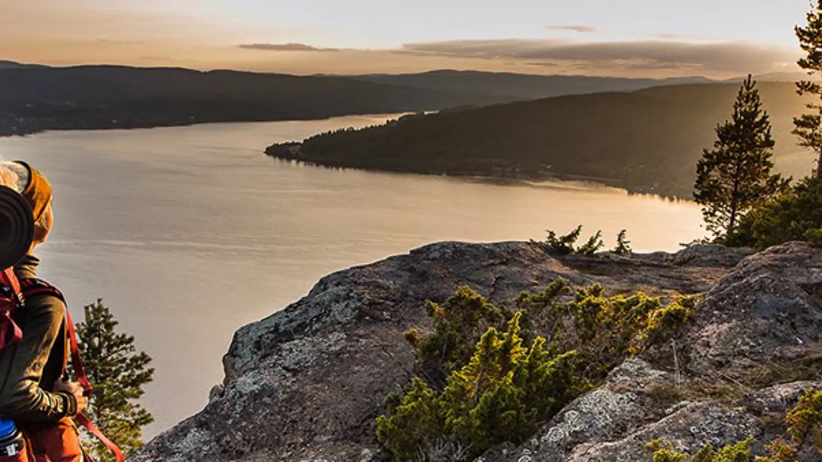 En kvinna med vandrarutrustning går på ett berg med utsikt över en sjö