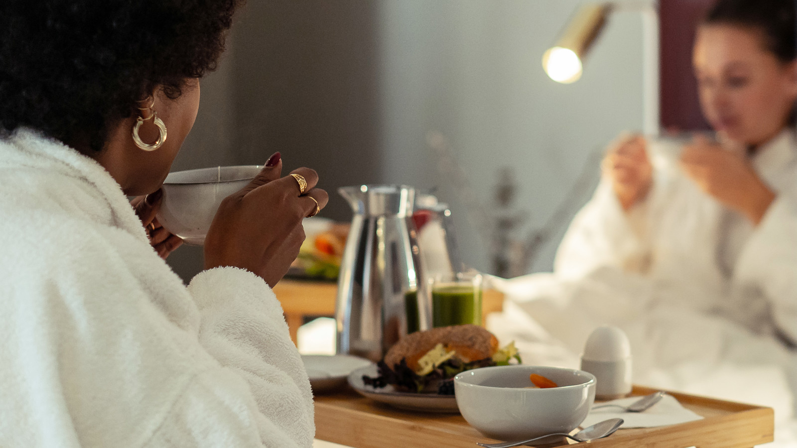 Två kvinnor i morgonrockar som äter frukost i hotellsäng