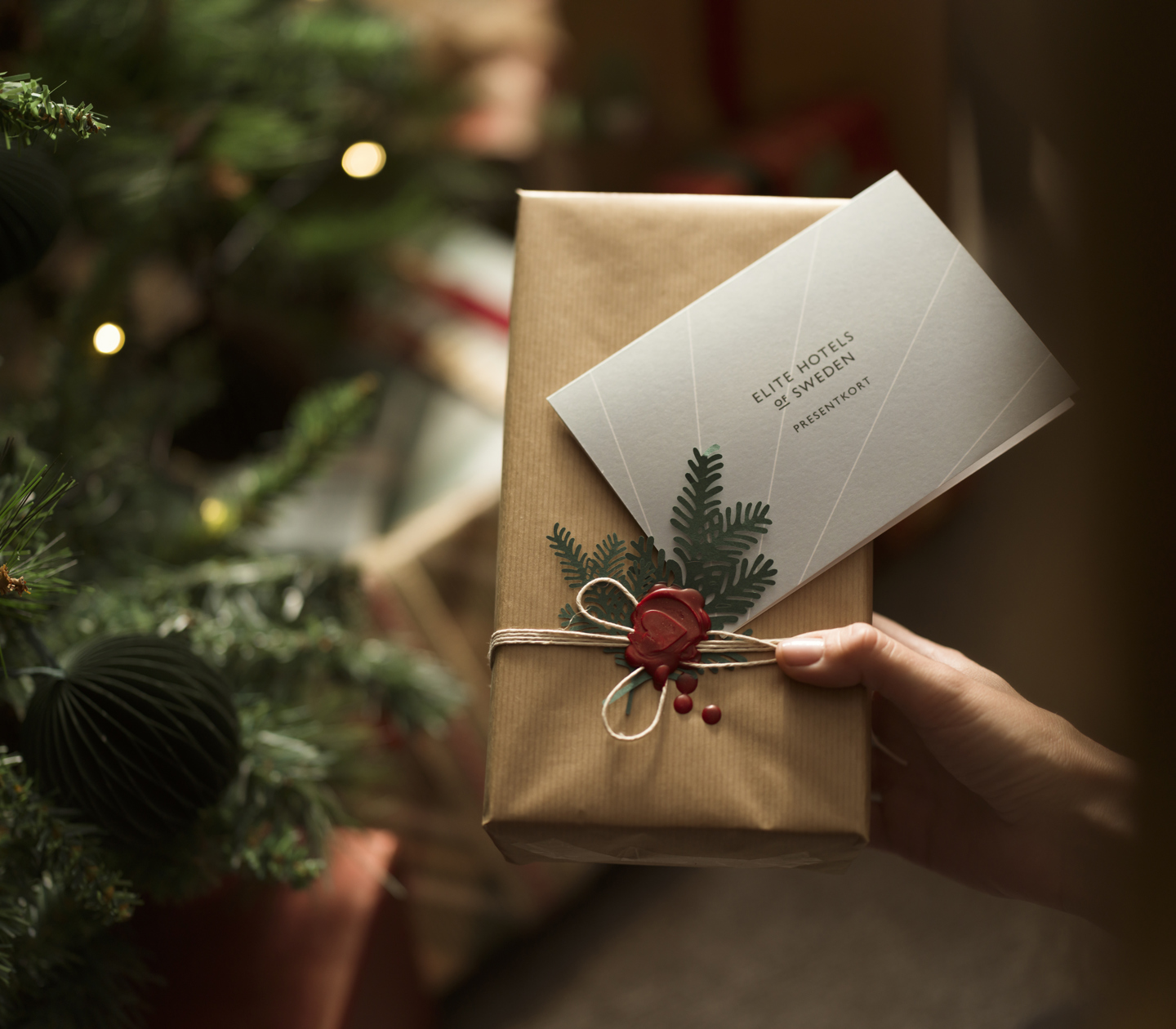Person som håller upp julklapp med presentkort framför julmiljö