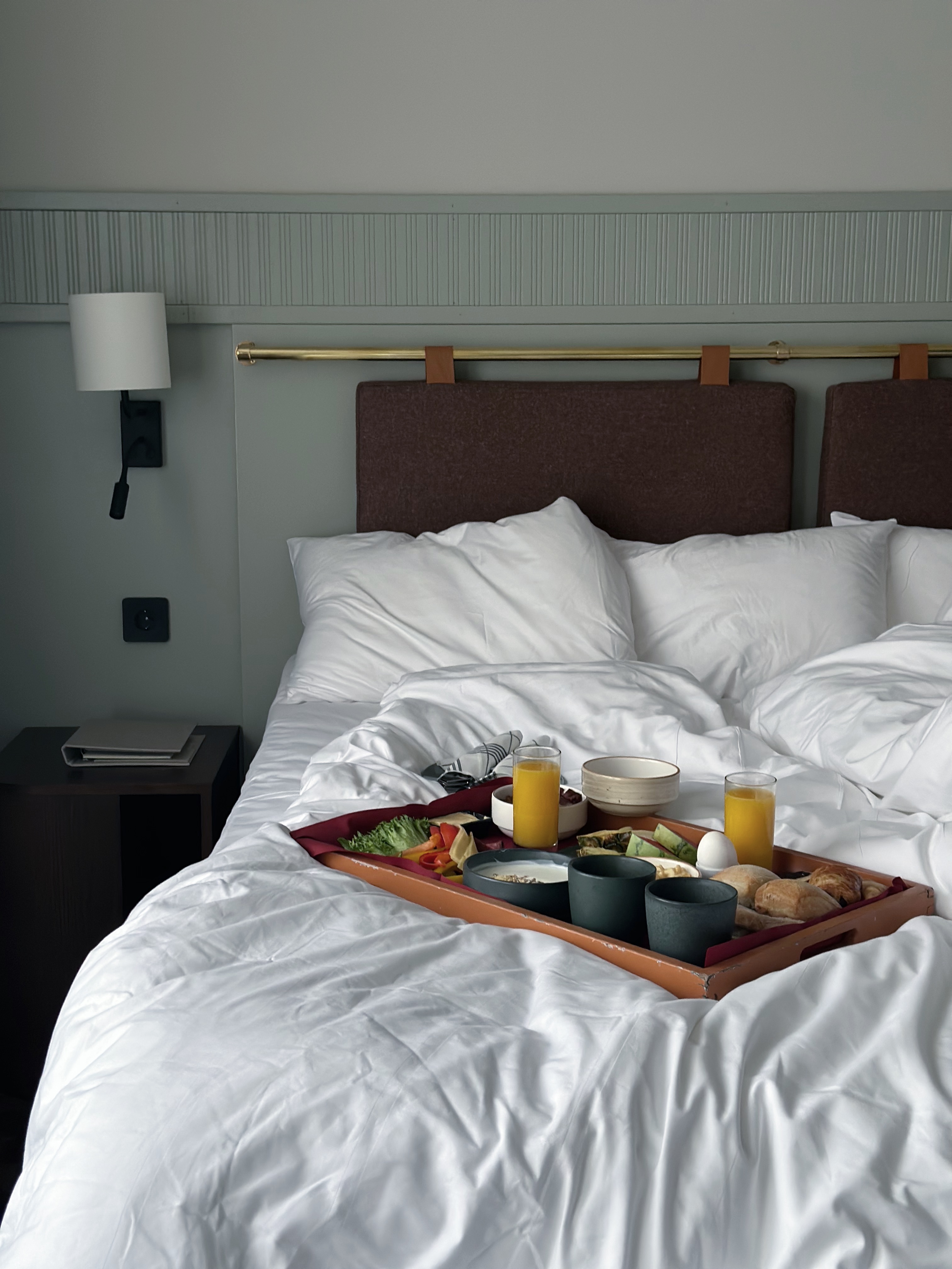 Breakfast tray in bed with juice, bread, and vegetables in a hotel room