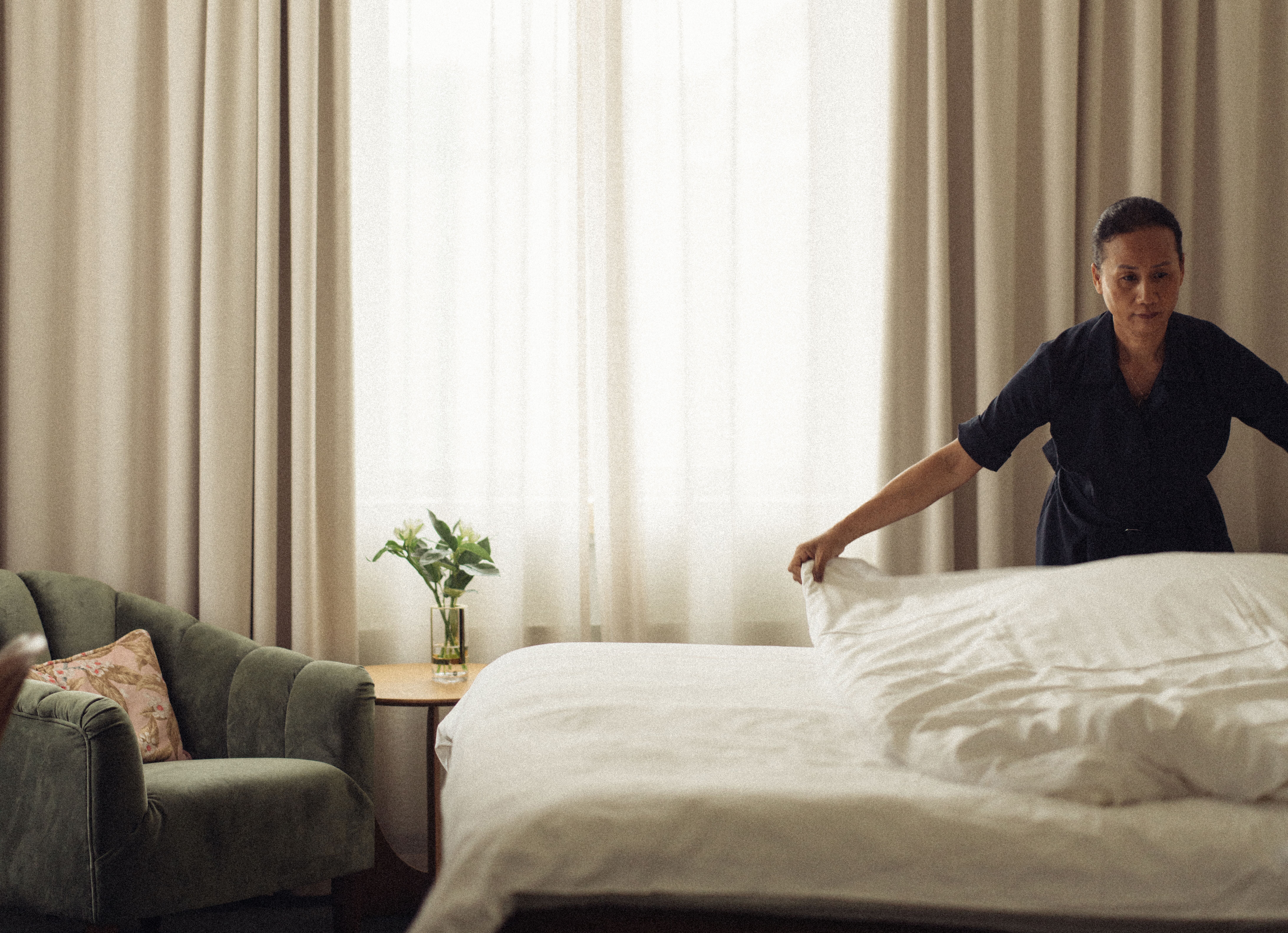 En person bäddar en säng i ett ljust sovrum.