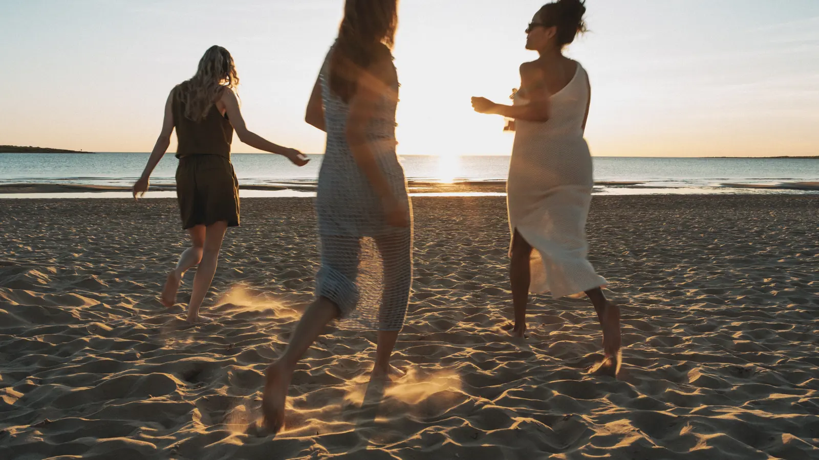 Tre kvinnor liggandes på strand framför havet