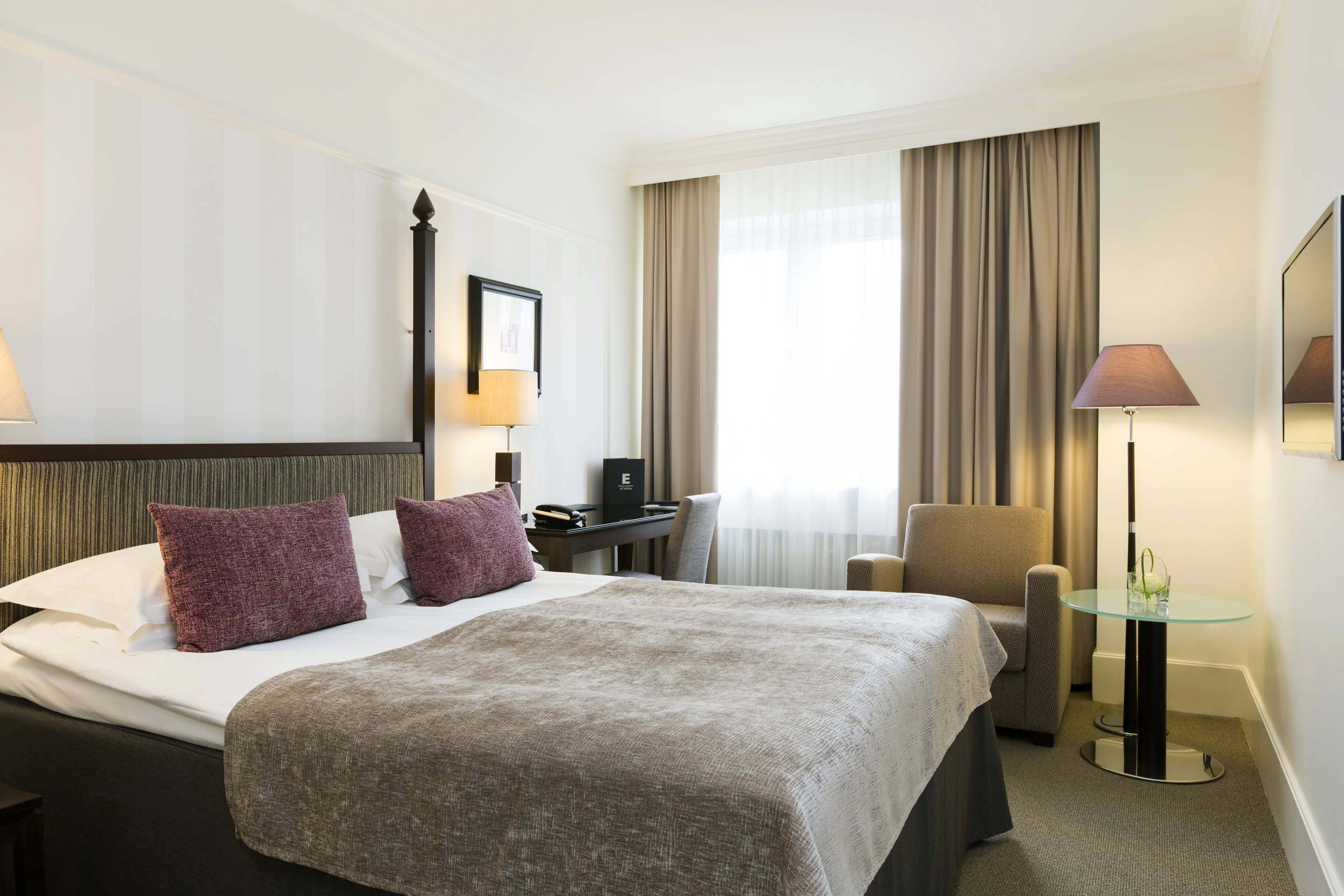 Mysigt hotellrum med dubbelsäng, skrivbord och fåtölj