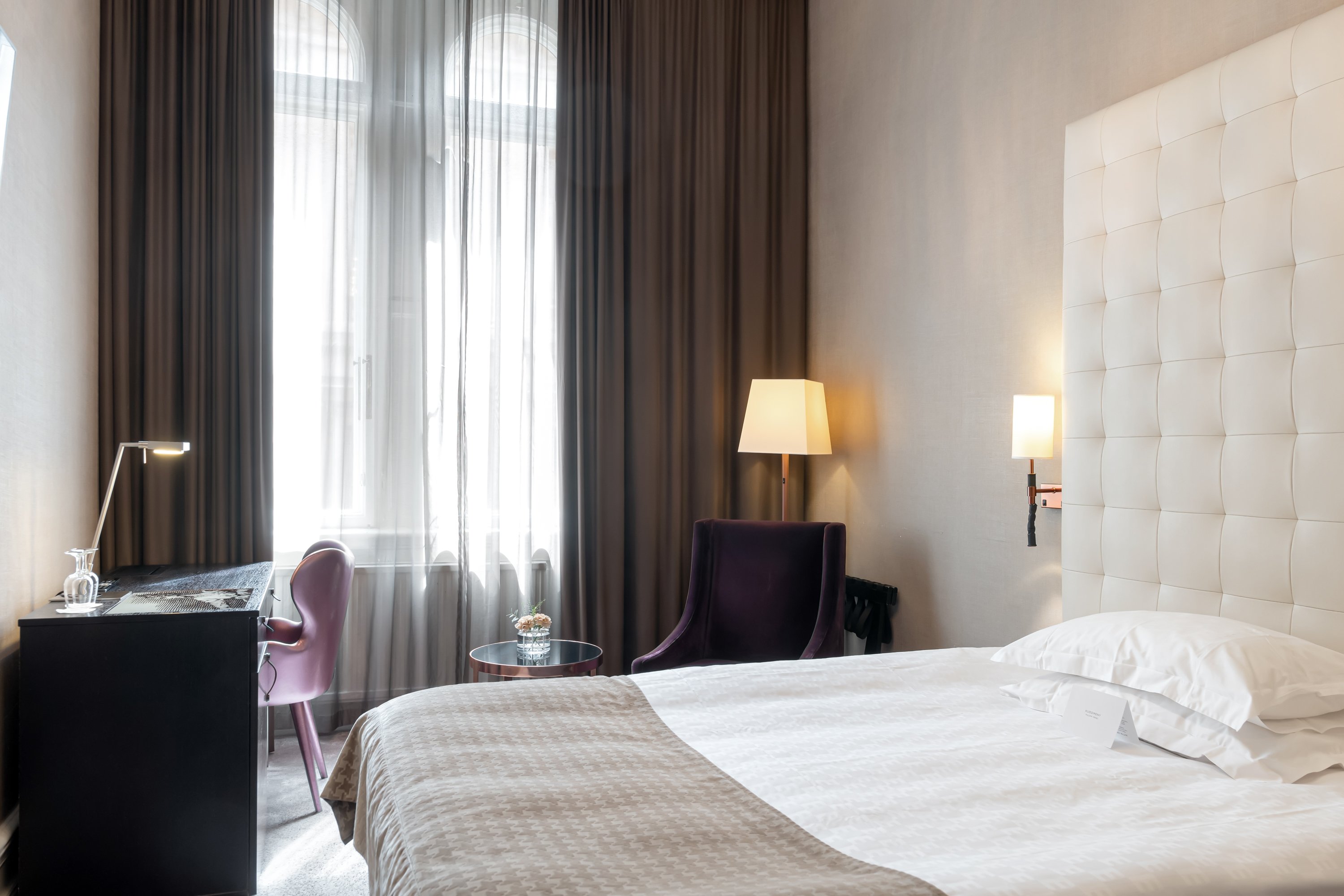 Bright hotel room with bed, large headboard and desk