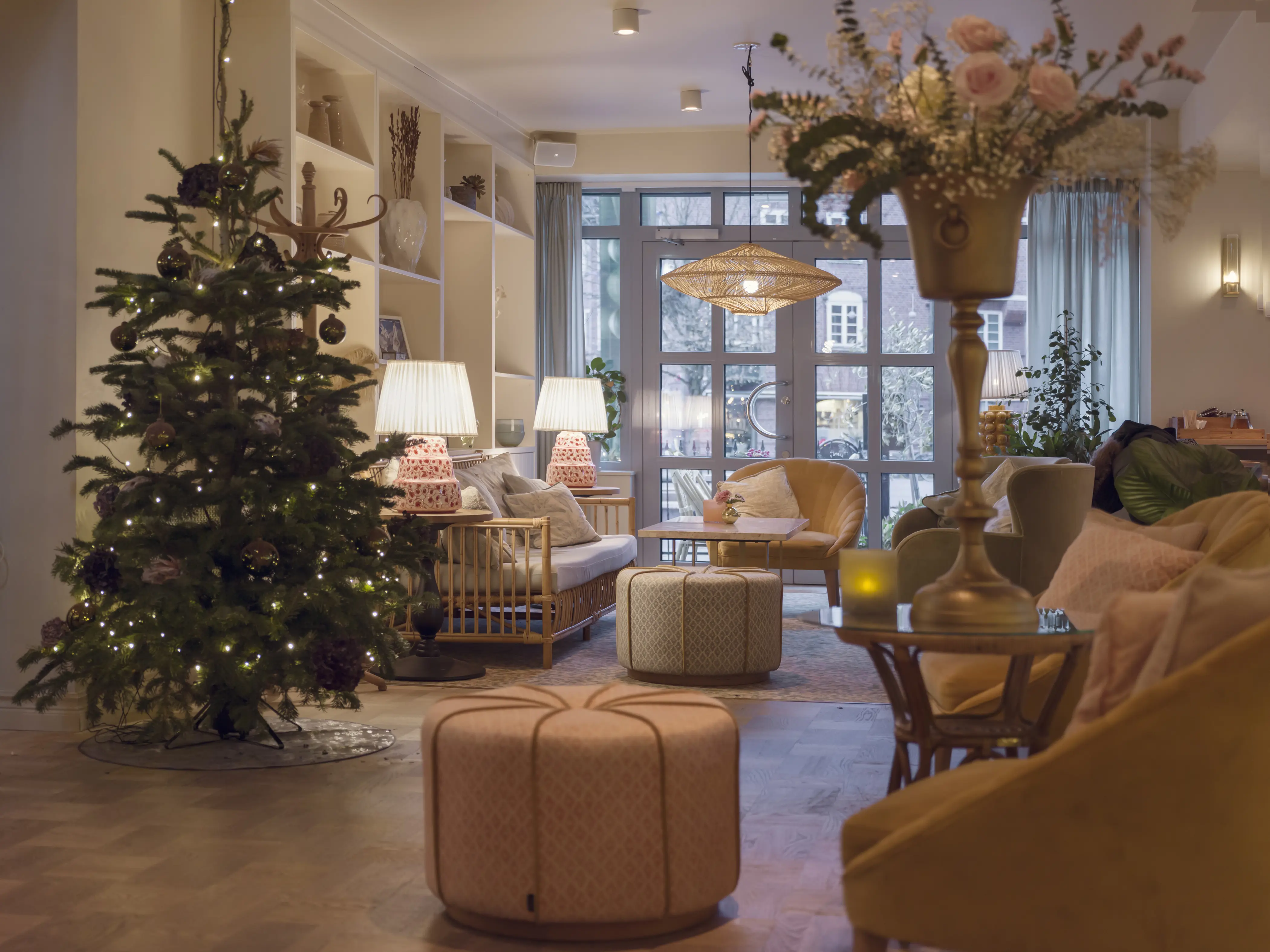 Cozy living room with Christmas tree, ambient lighting, and elegant decor, featuring soft seating, a centerpiece table, and large windows overlooking a winter scene.