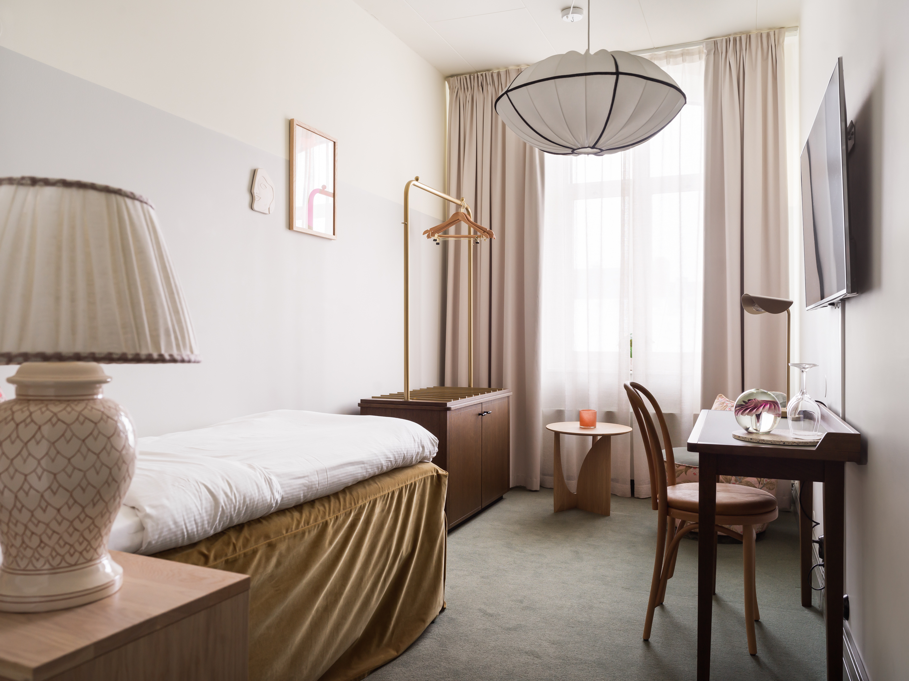 Sänglampa, del av enkelsäng och skrivbord i hotellrum