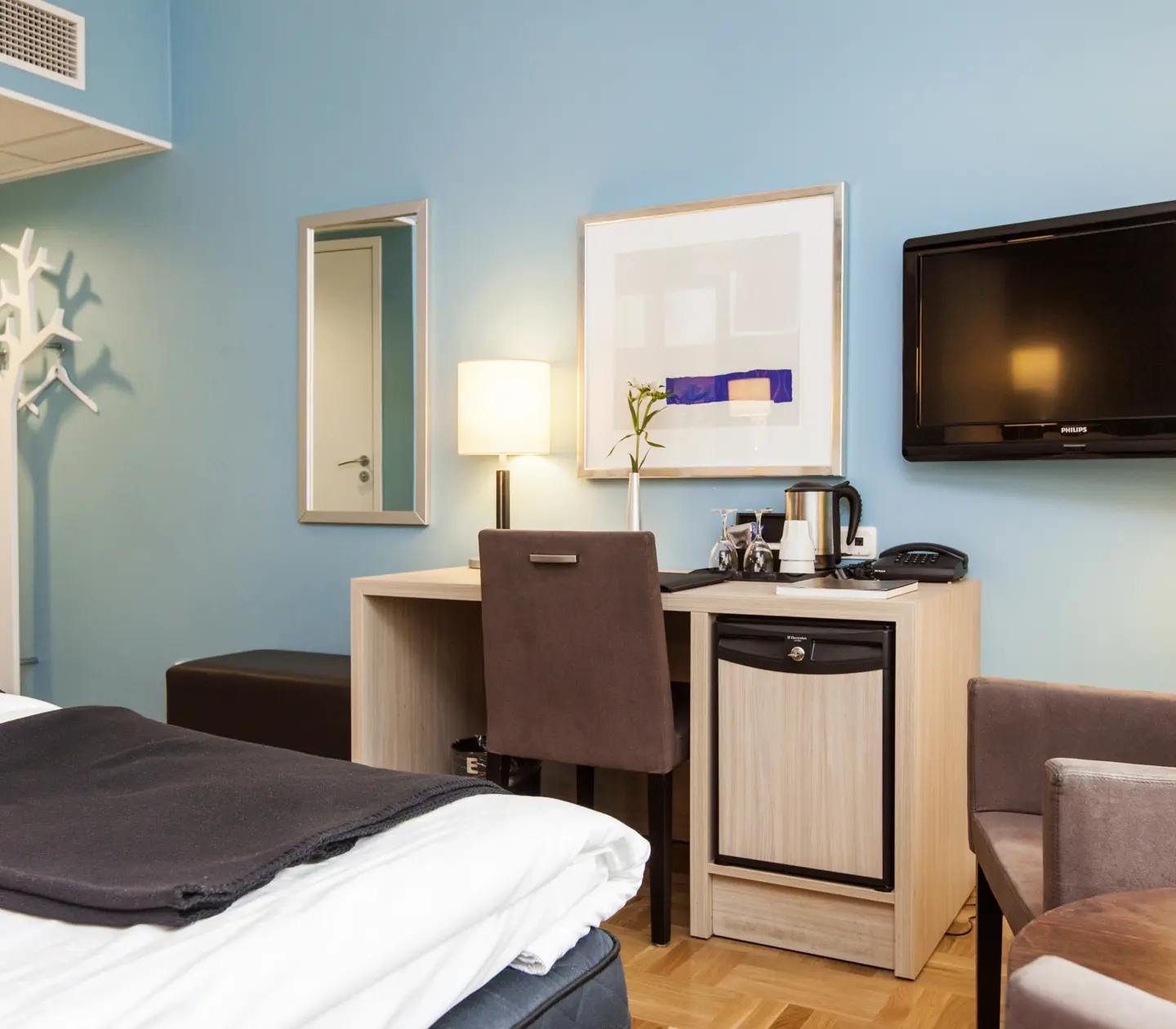 Ljust hotellrum med blå vägg, tv och skrivbord