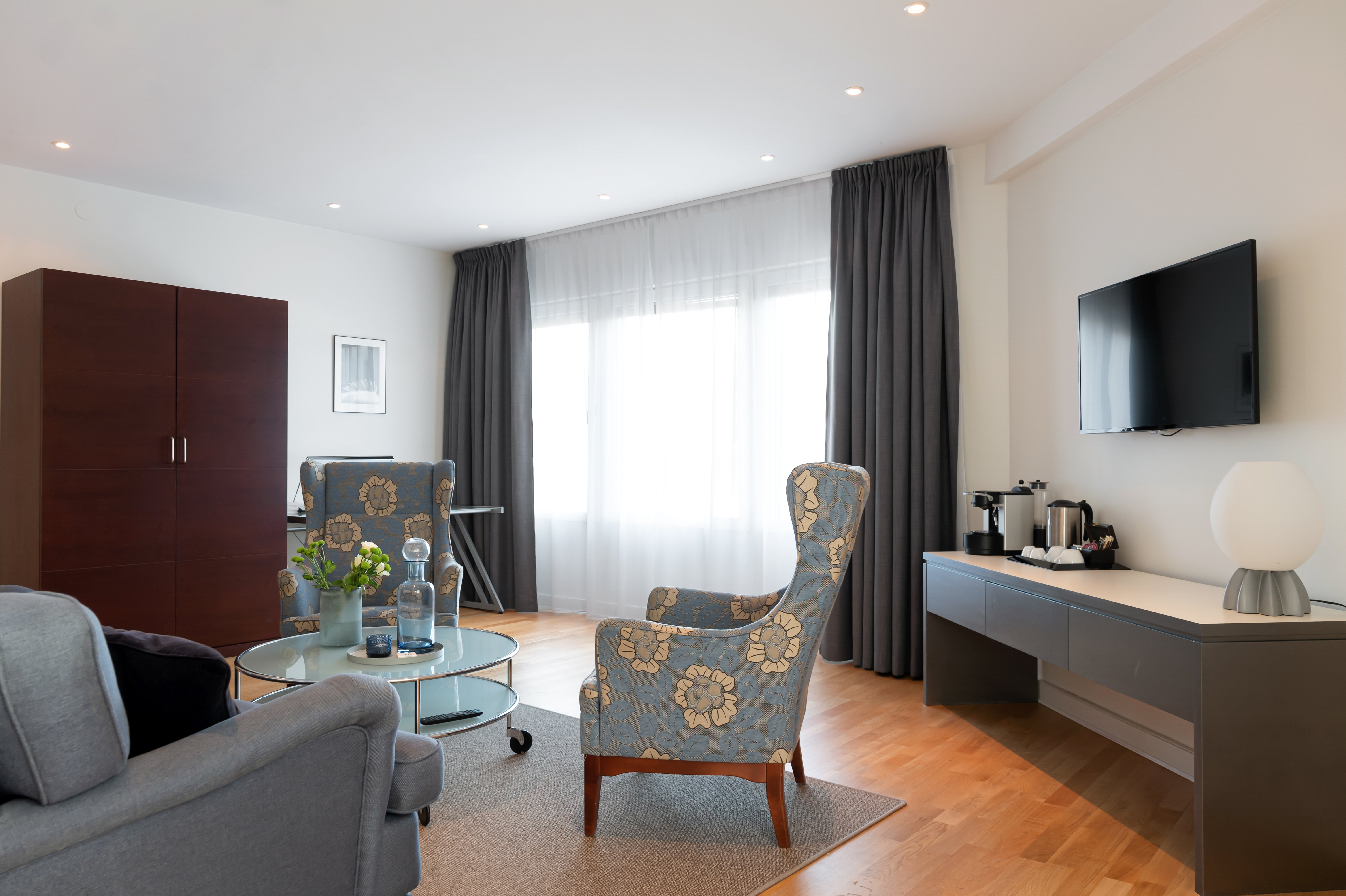 Bright hotel suite with sofa group, TV and wardrobe