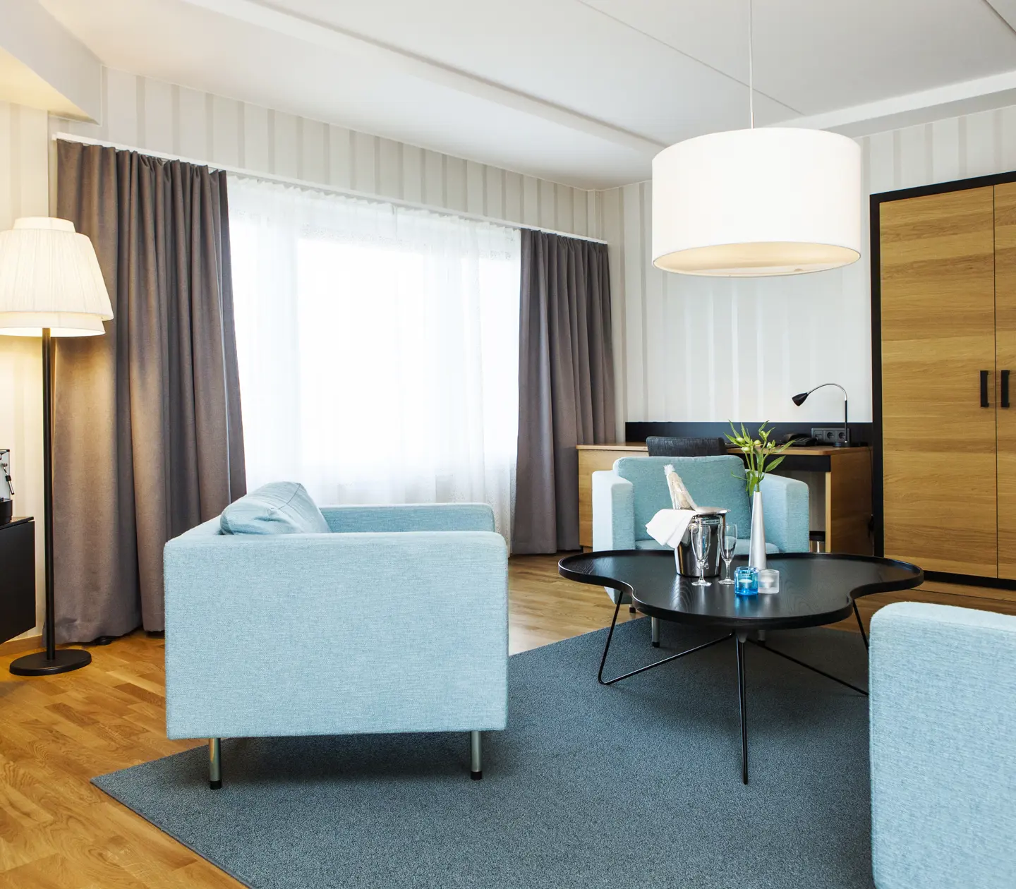 Hotellsvit med blå soffgrupp, skrivbord och garderob