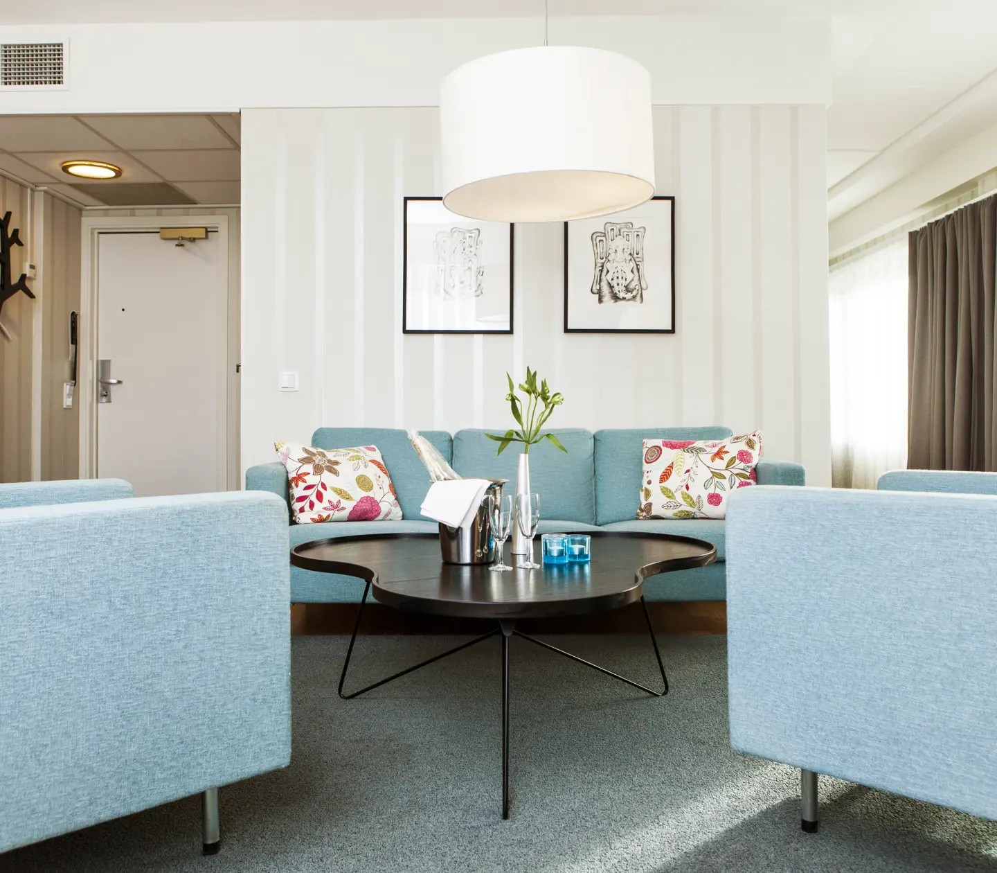 Ljus hotellsvit med blå soffgrupp, fönster och tavlor