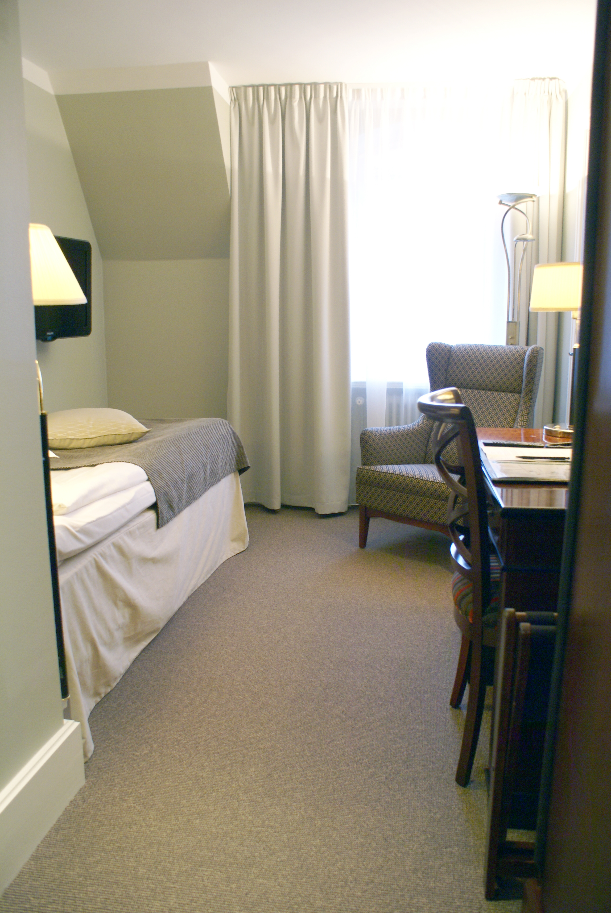 Hotellrum med enkelsäng, fåtölj och skrivbord