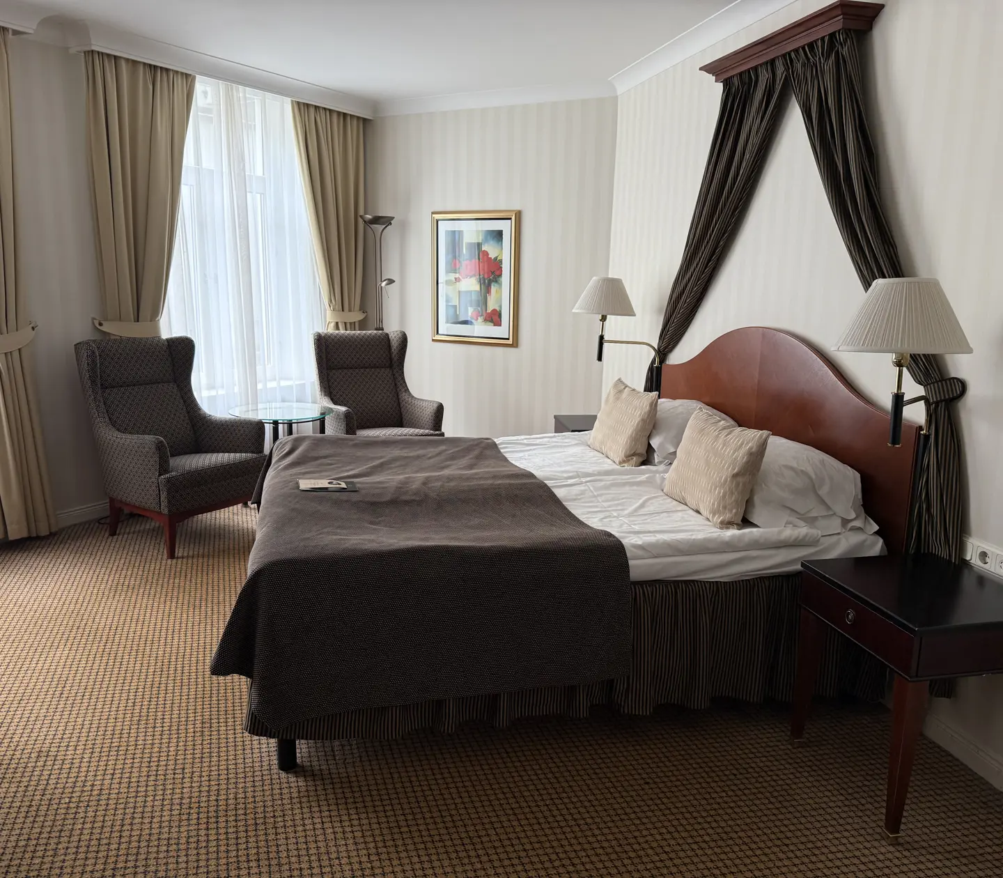 Lyxigt hotellrum med en dubbelsäng, eleganta sittplatser och stora fönster med gardiner.