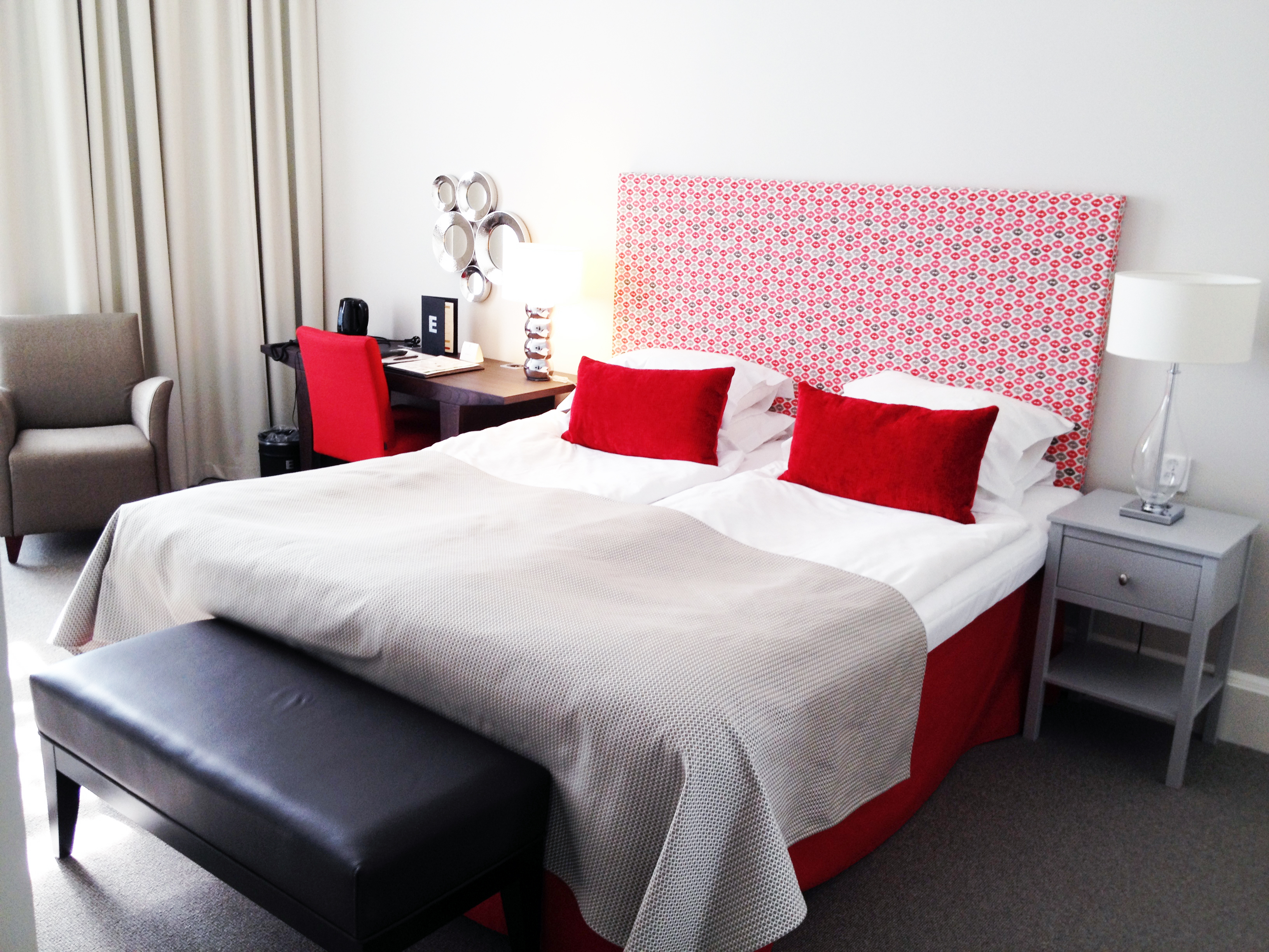 Hotellrum med dubbelsäng, röd sänggavel och skrivbord