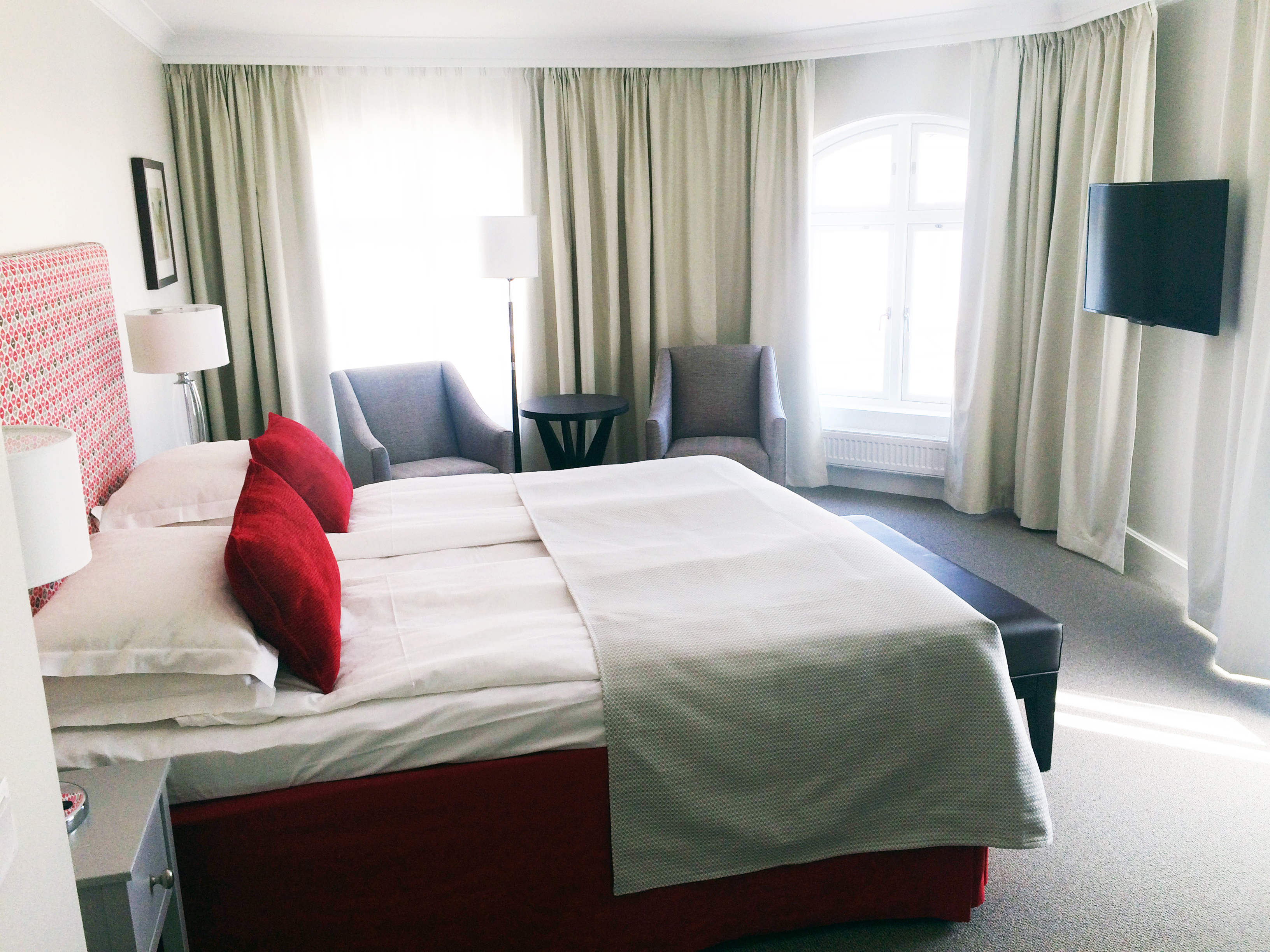 Hotel room with double bed, red headboard and armchairs