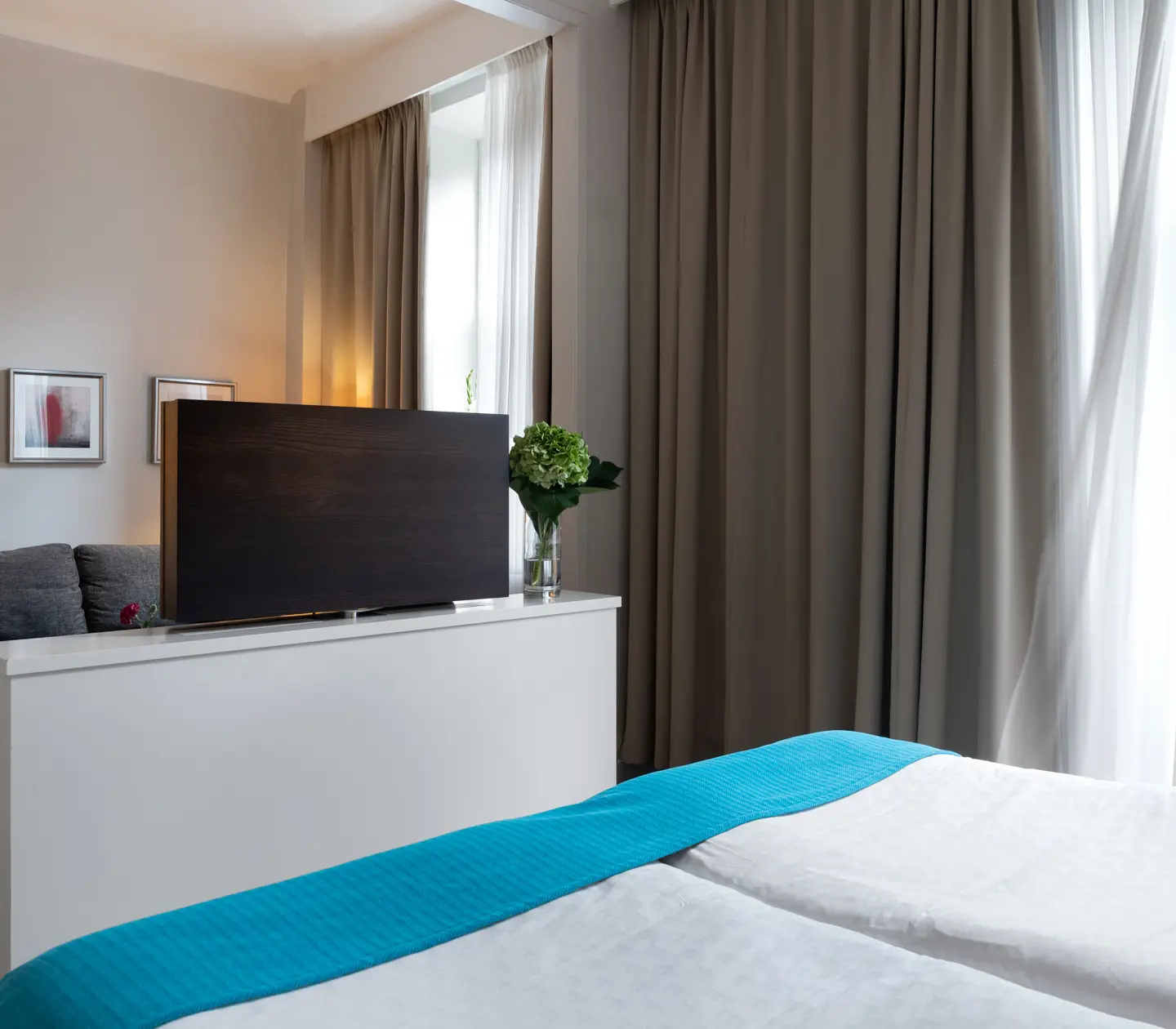 Ljust hotellrum med soffa, tv och stora fönster