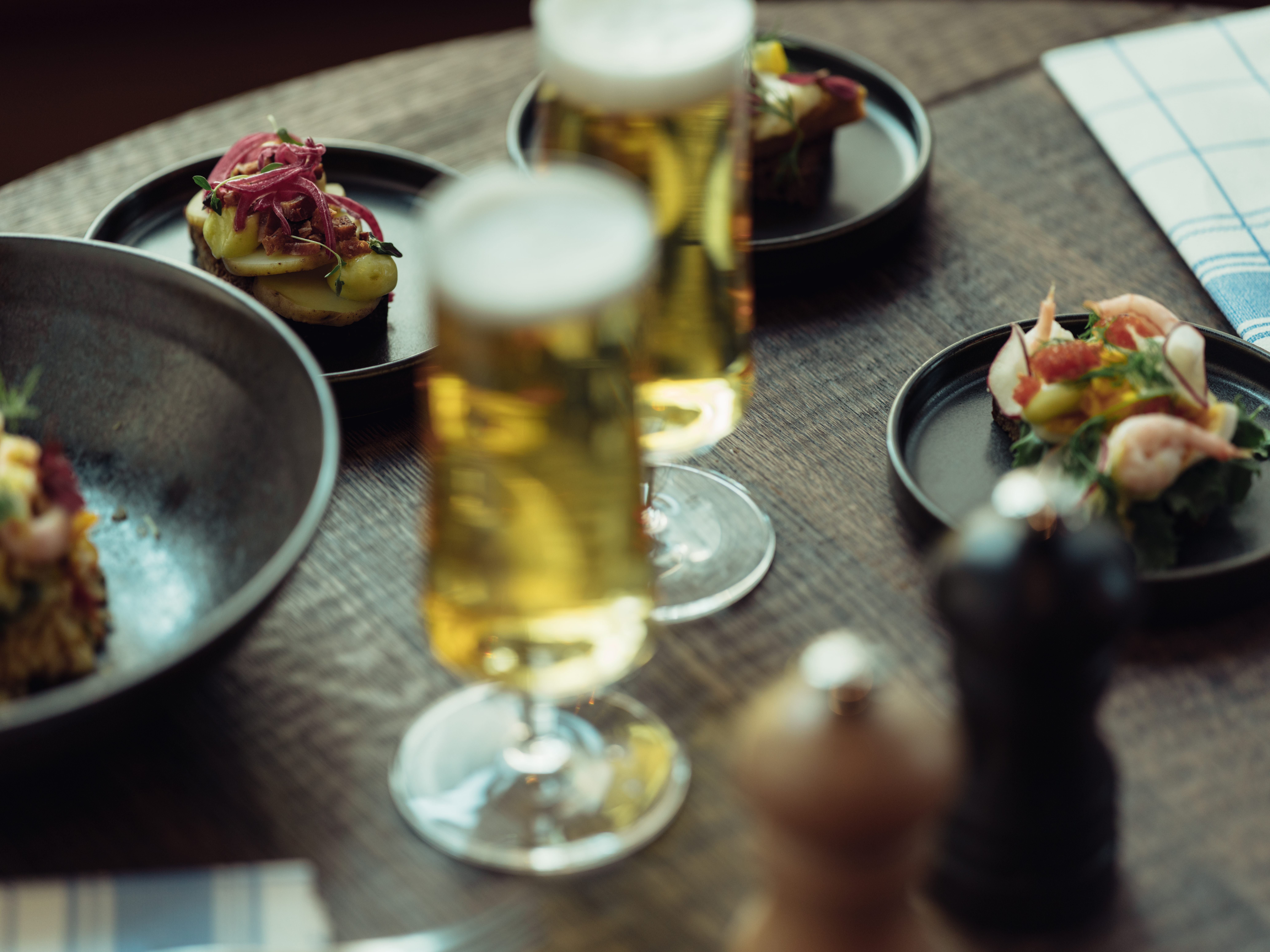 Traditionella svenska smörgåsar med skaldjur och inlagd rödlök serverade med glas öl på ett träbord.