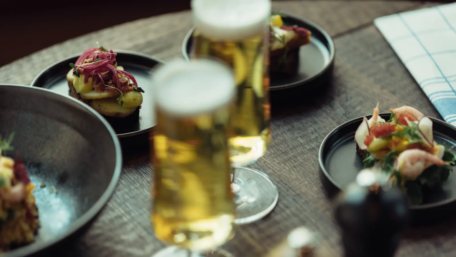 Traditionella svenska smörgåsar med skaldjur och inlagd rödlök serverade med glas öl på ett träbord.