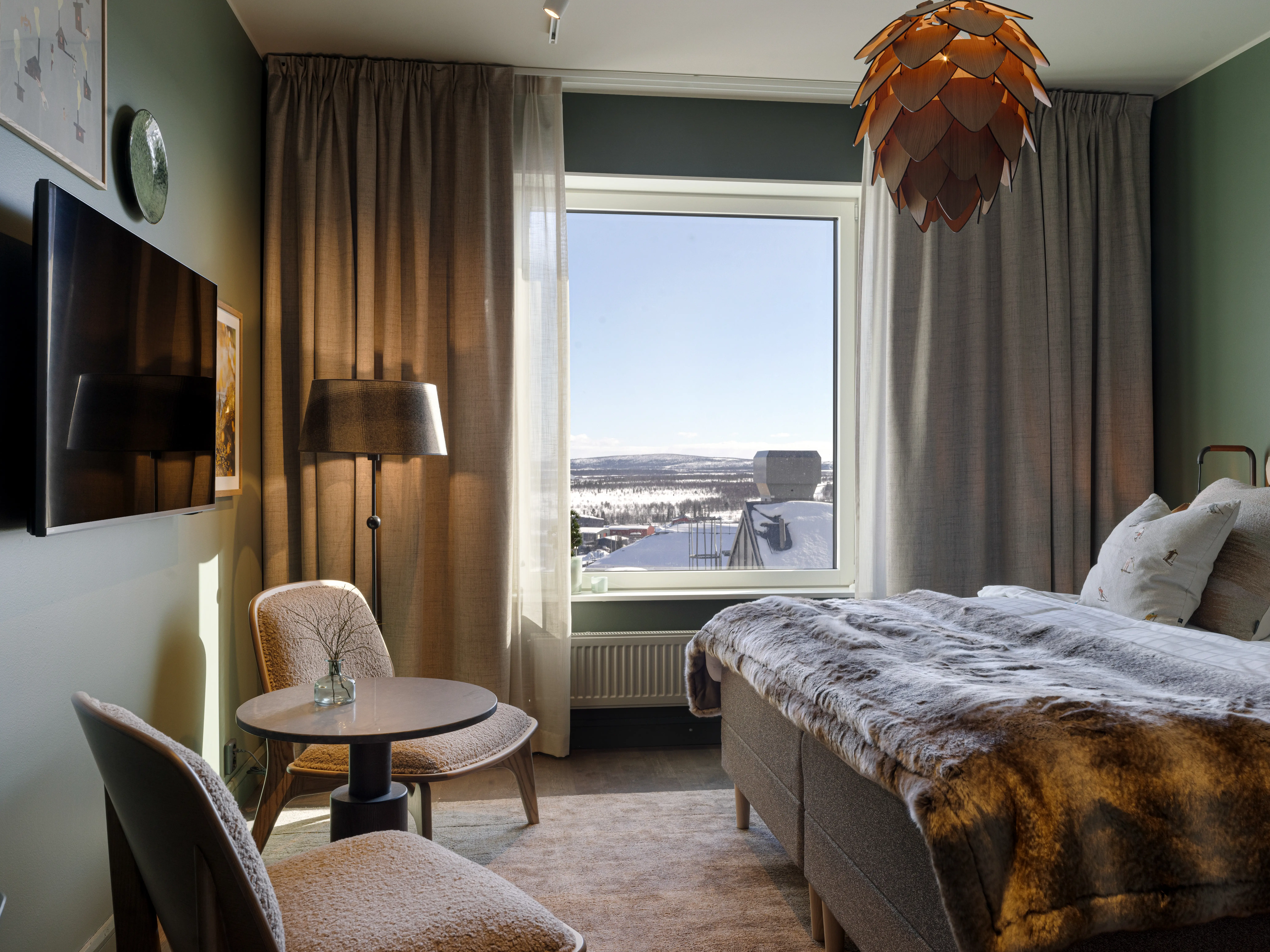 Cozy hotel room with bed, ceiling lamp, window, and armchairs.