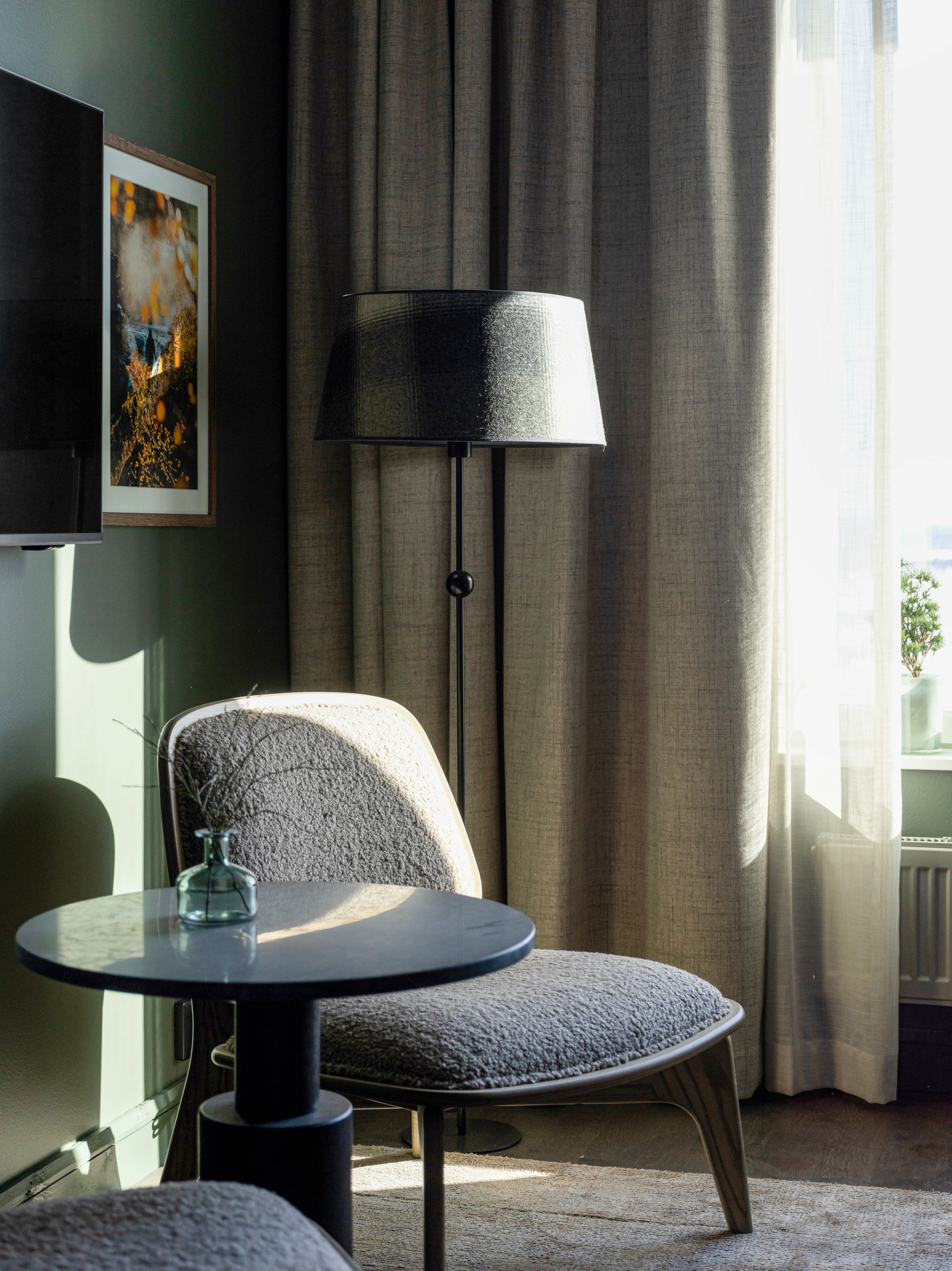Cozy hotel room with armchair, floor lamp, and curtains.