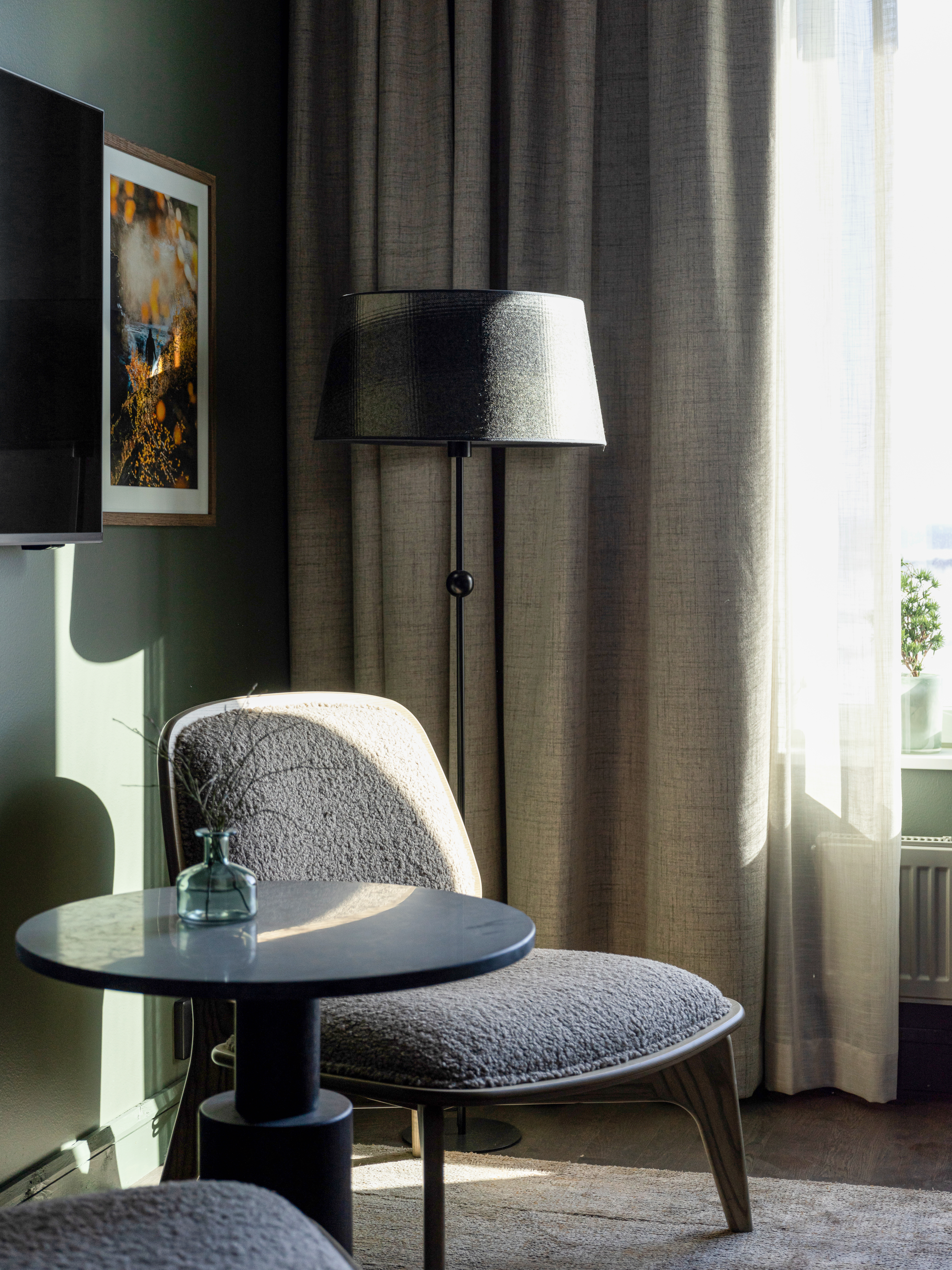 Mysigt hotellrum med fåtölj, golvlampa och gardiner