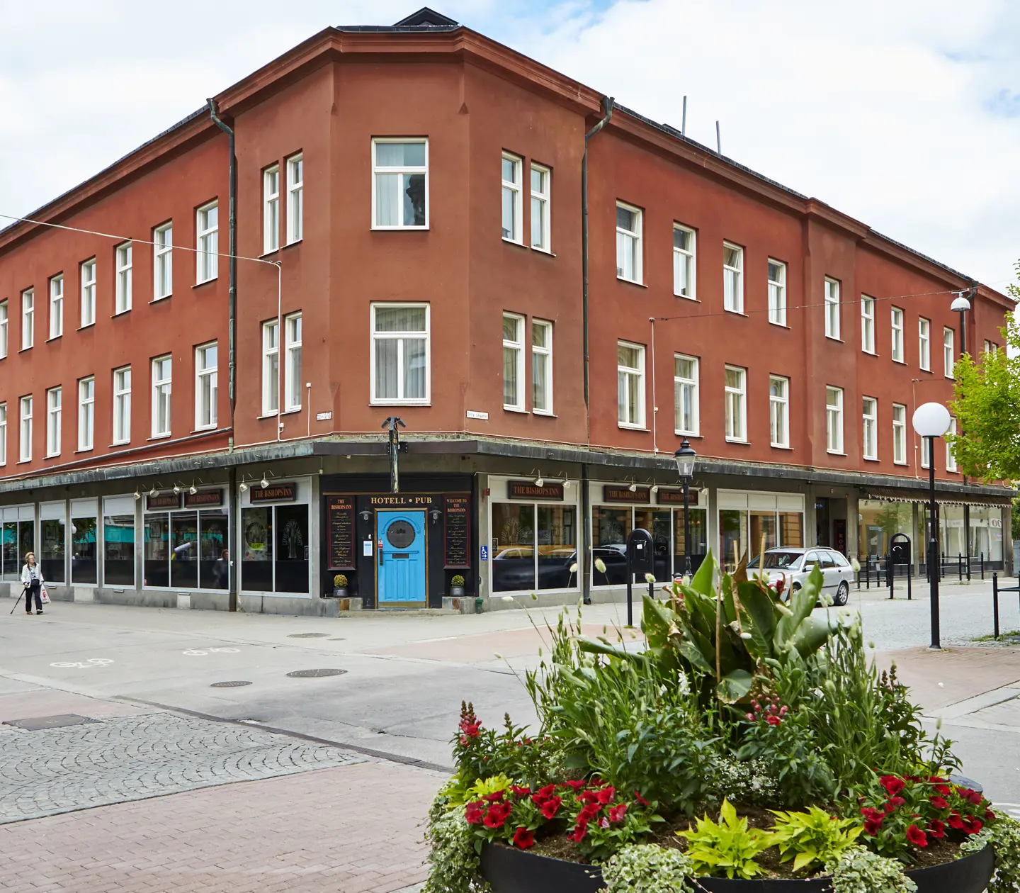 Fasaden av Hotel Bishops Arms med bilväg och blomsterplanteringar framför