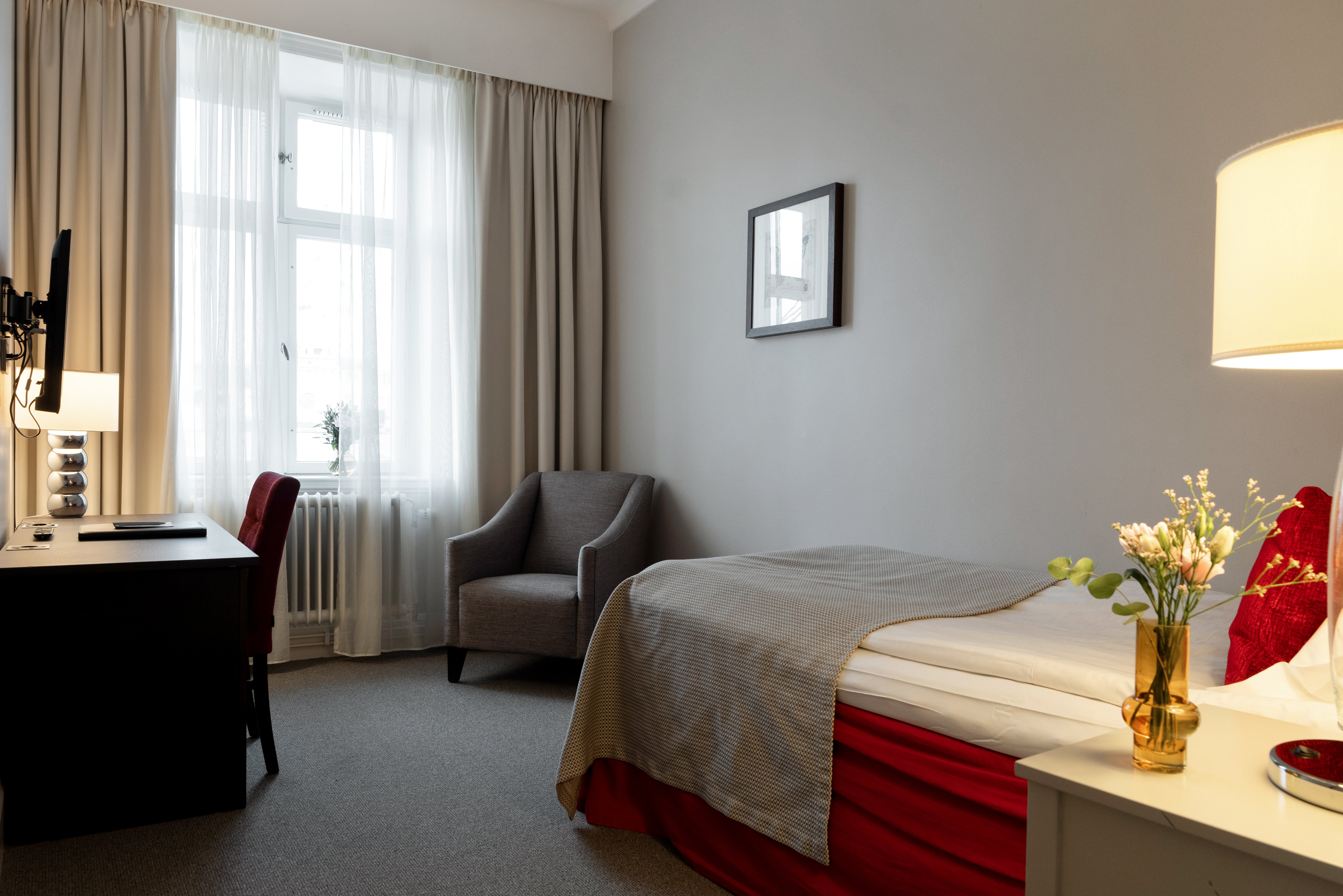 Mysigt hotellrum med enkelsäng, röd sänggavel, nattduksbord och spegel