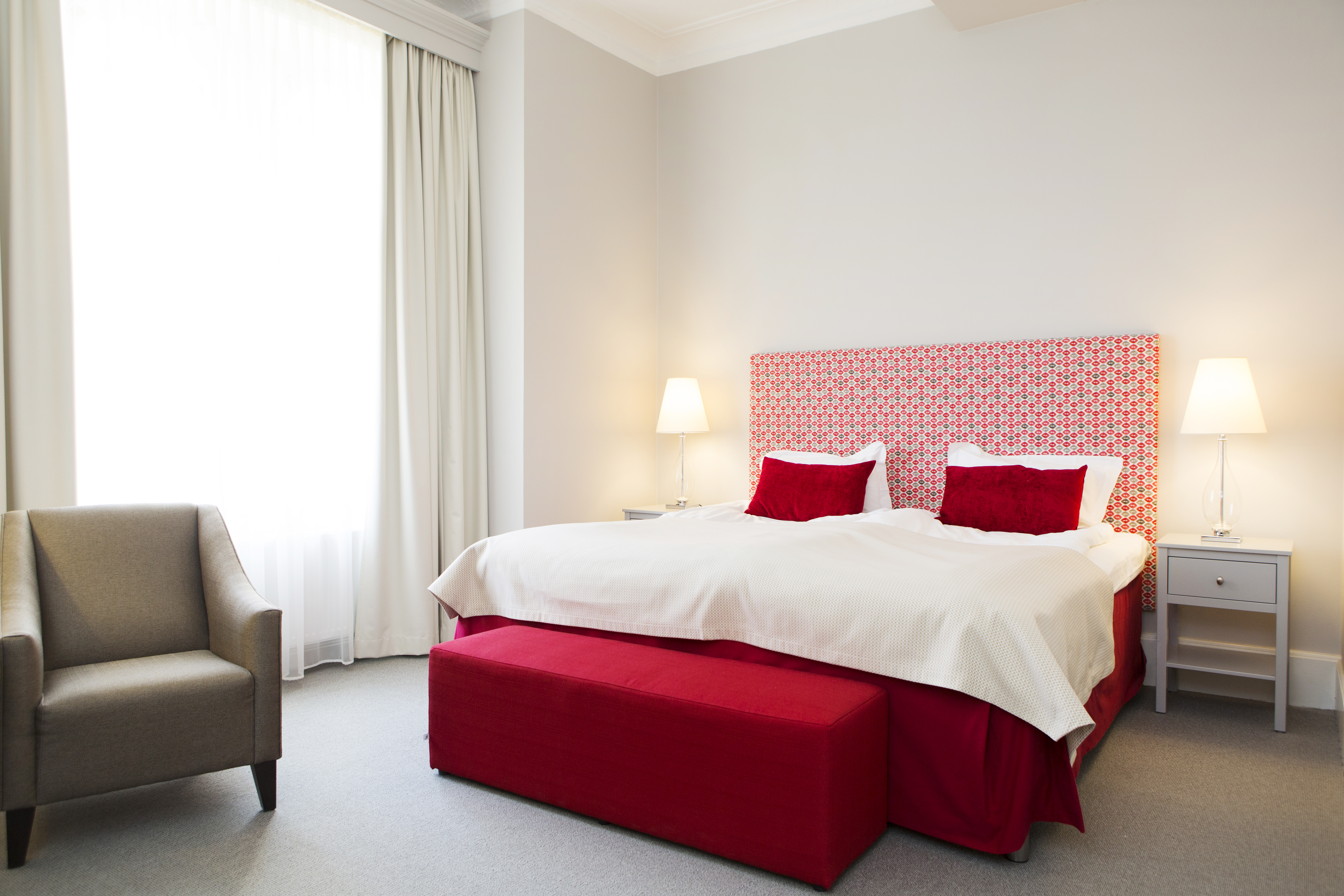 Bright hotel room with bed, red headboard and armchair