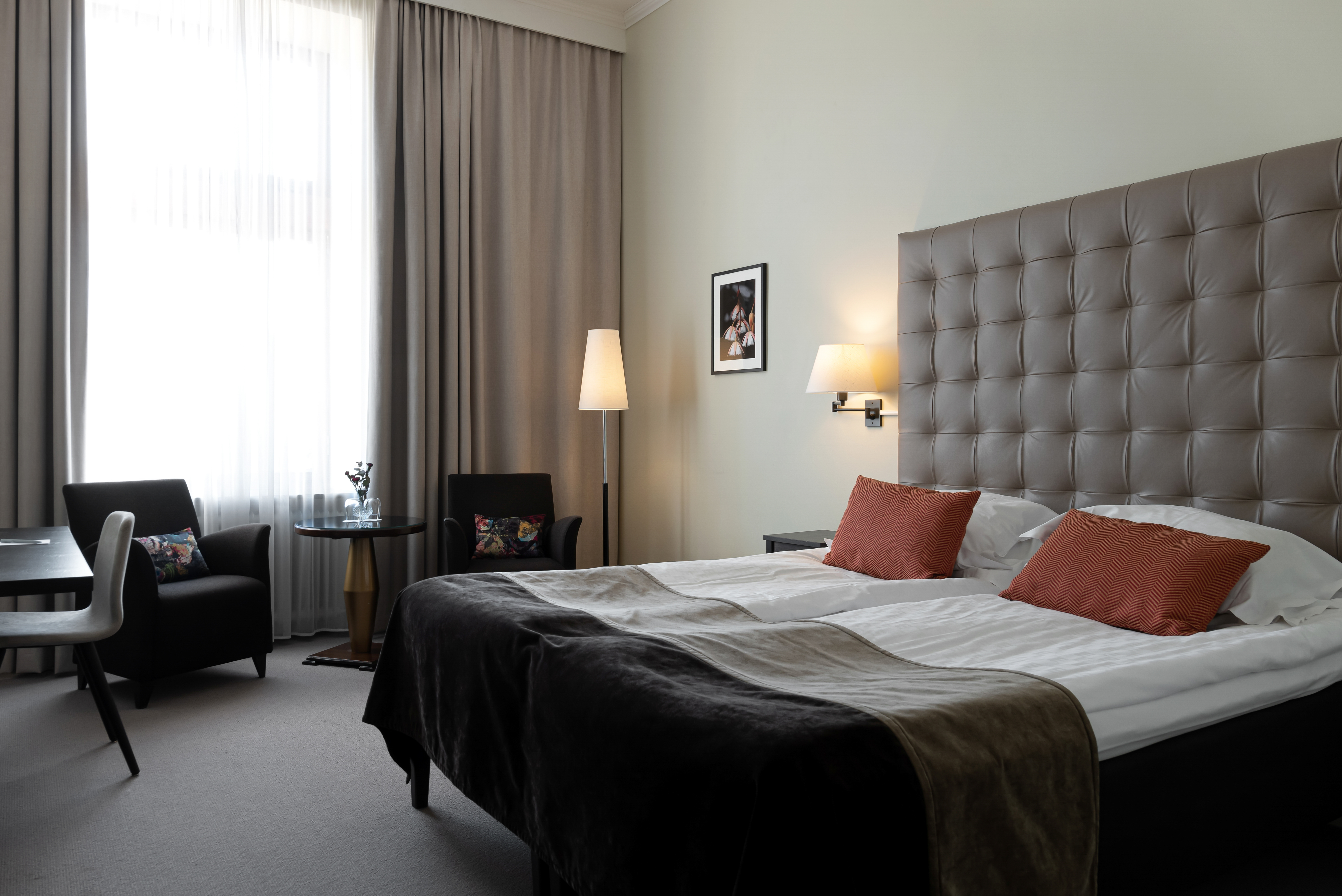 Bright hotel room with bed, large headboard and armchairs